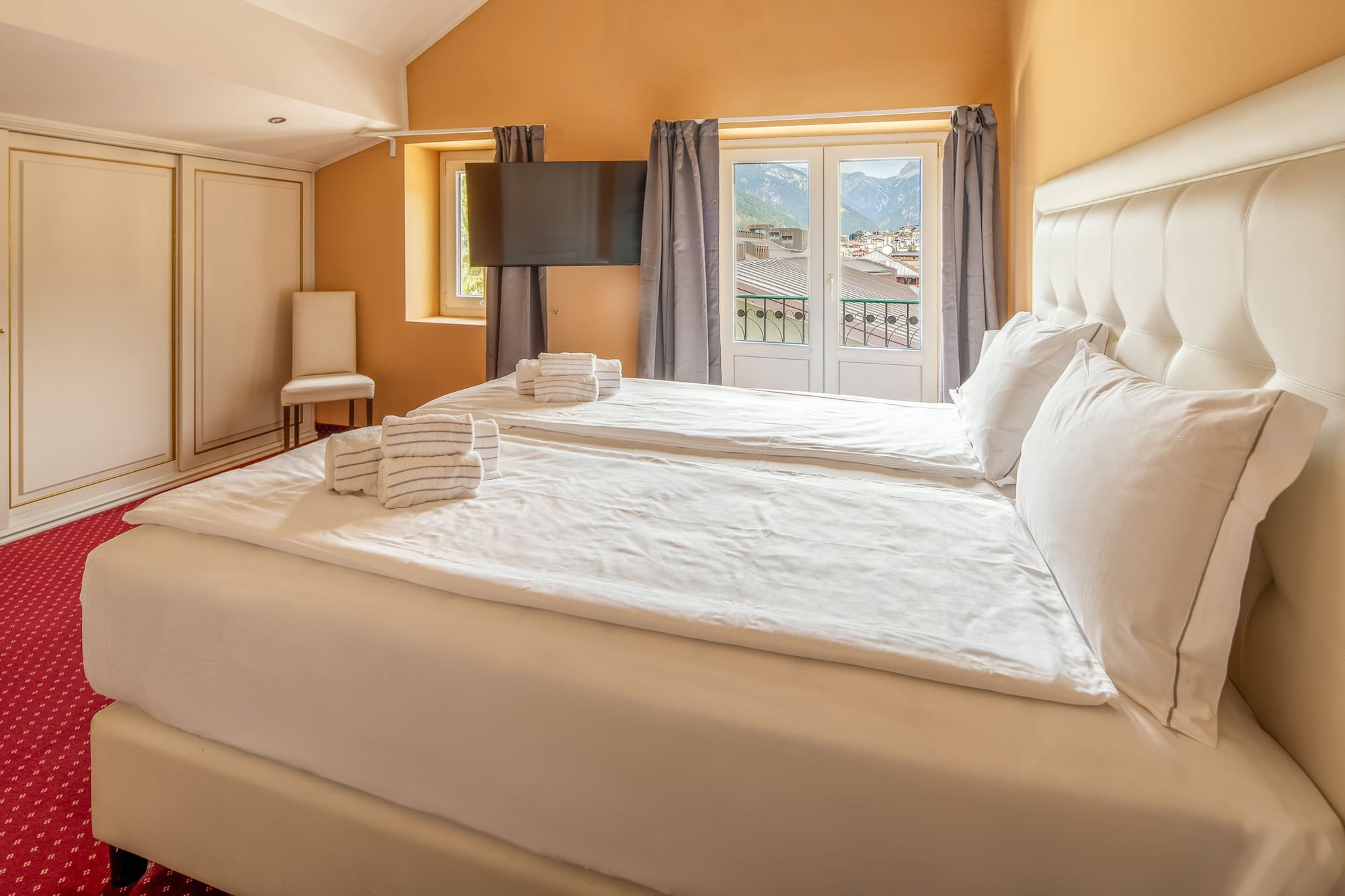 Hotel bedroom with twin beds, white bedding, and balcony mountain view.