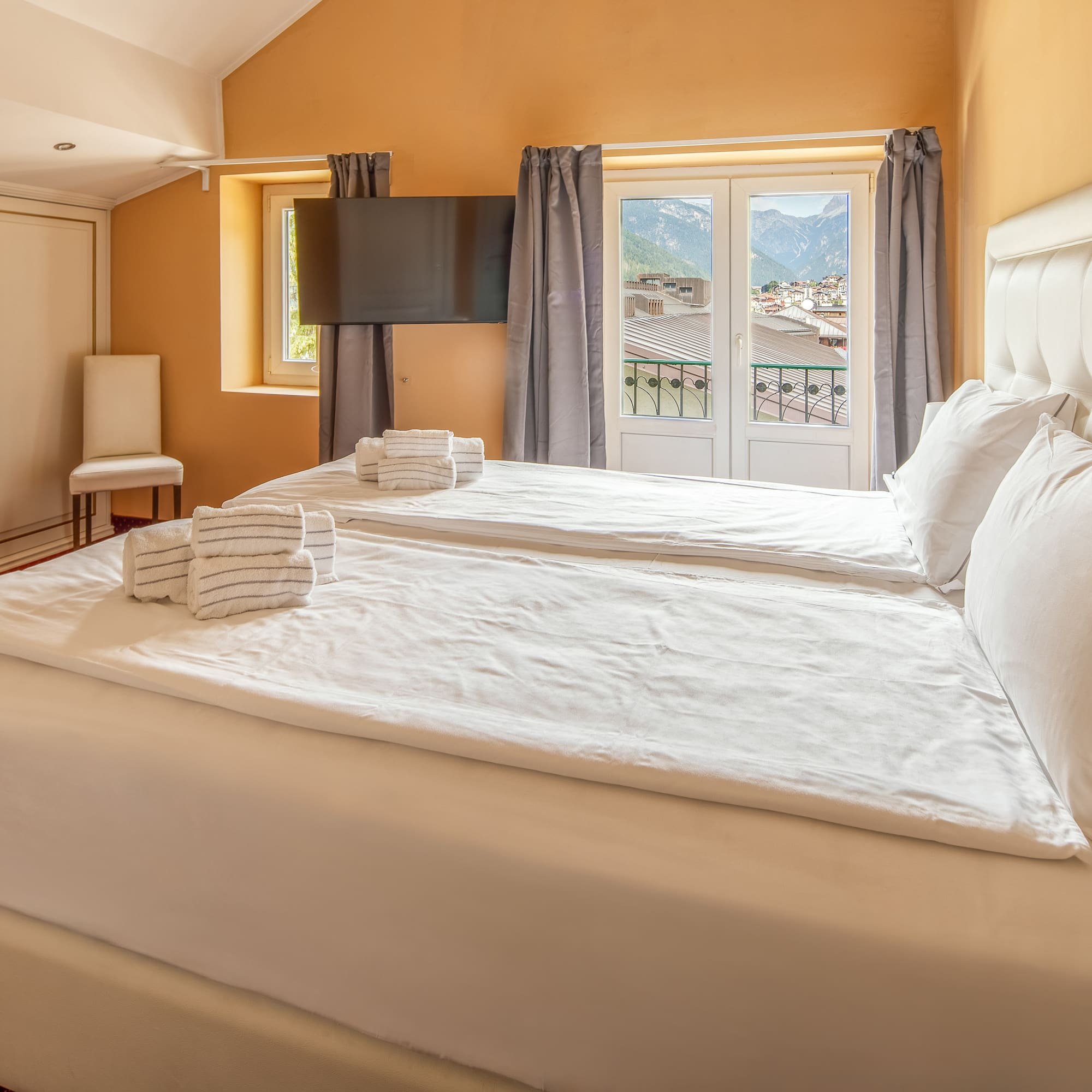 Hotel bedroom with twin beds, white bedding, and balcony mountain view.