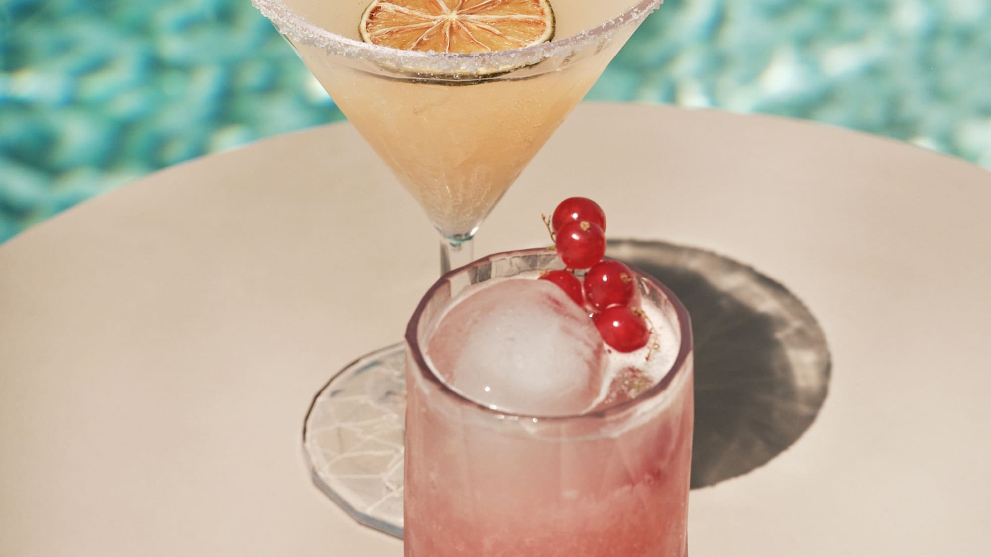Dos cócteles junto a la piscina: margarita con lima y bebida rosa con grosellas.