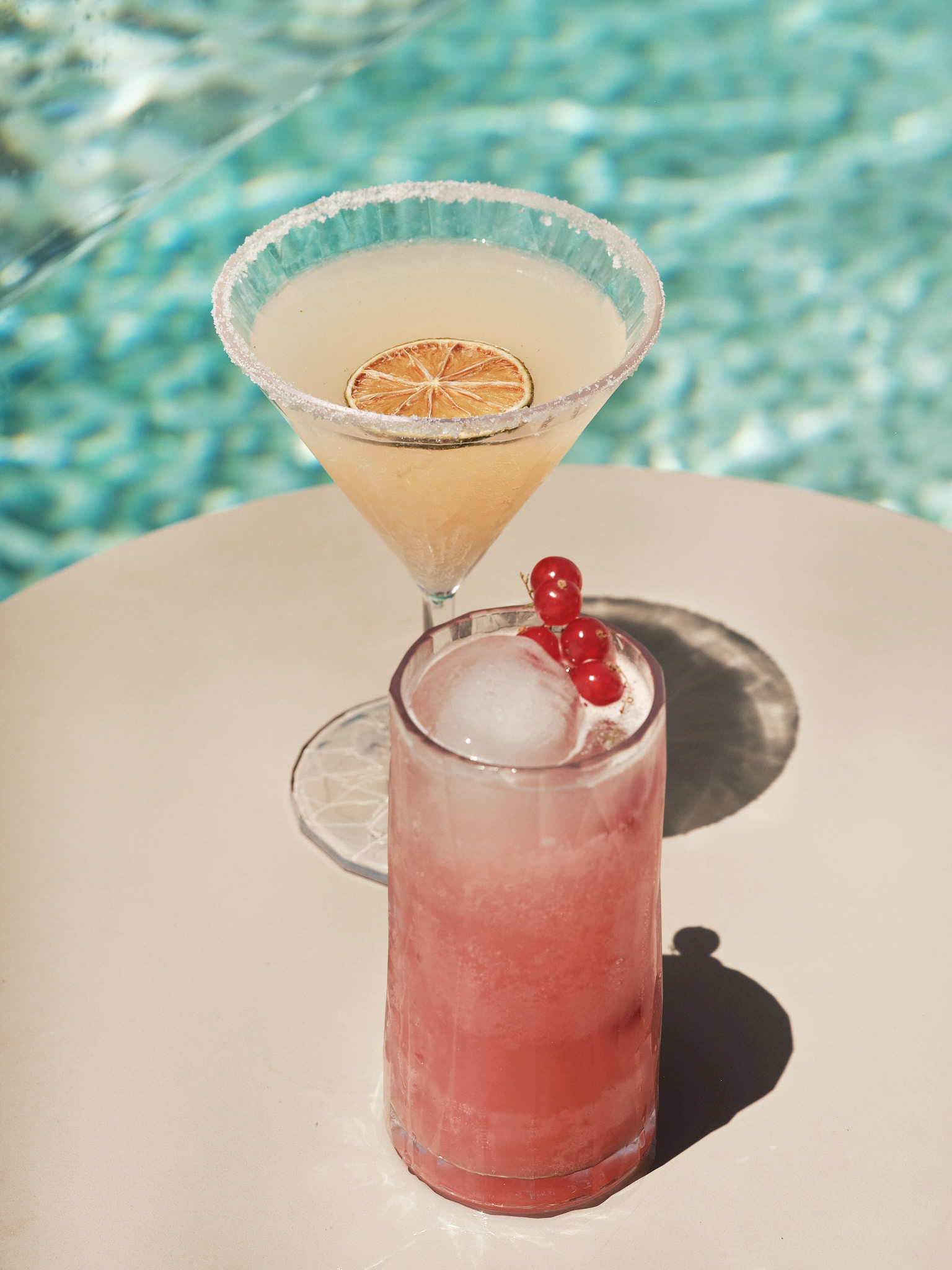 Dos cócteles junto a la piscina: margarita con lima y bebida rosa con grosellas.