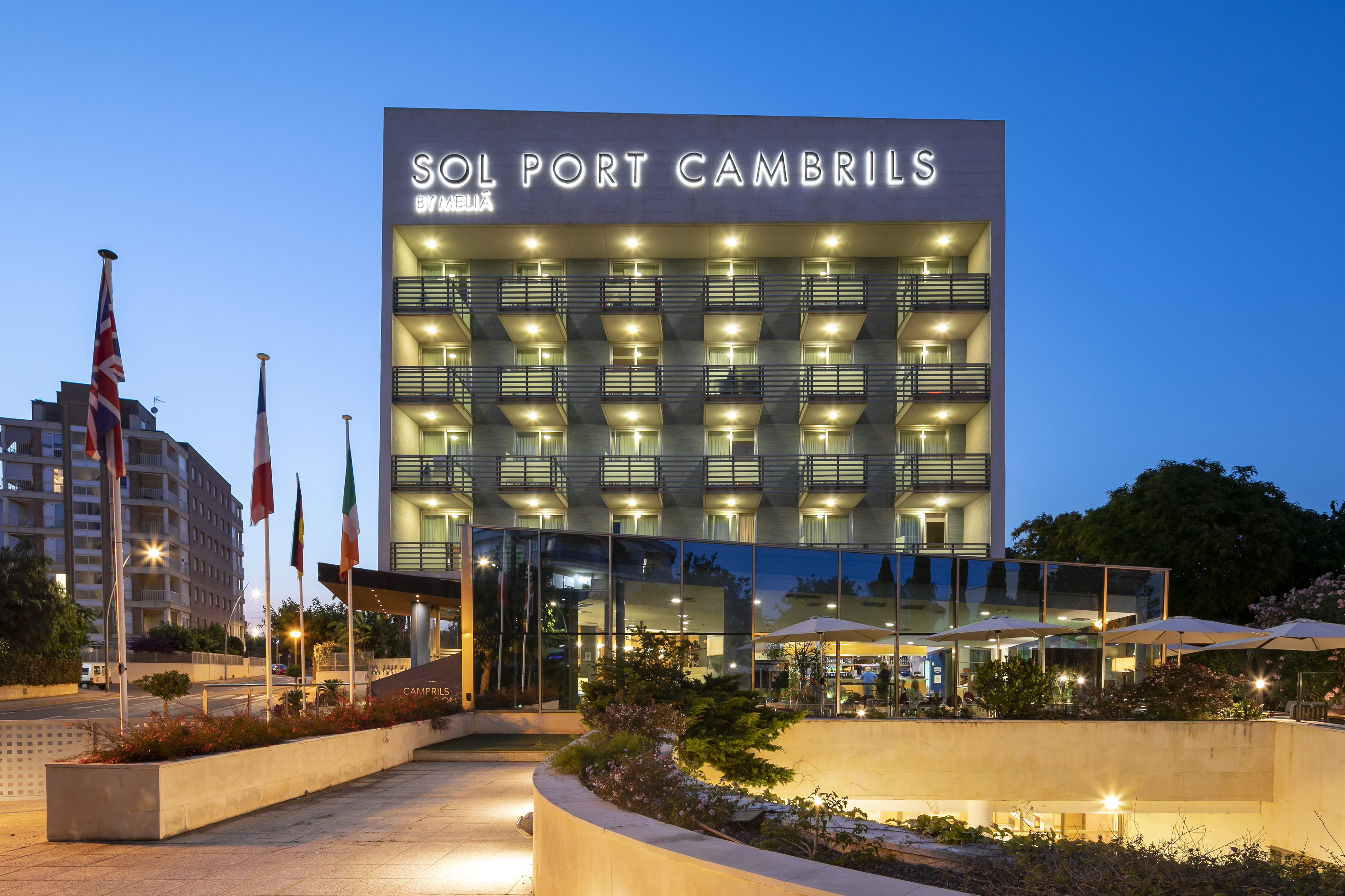 Sol Port Cambrils Meliá hotel exterior at dusk, with illuminated sign and balconies.