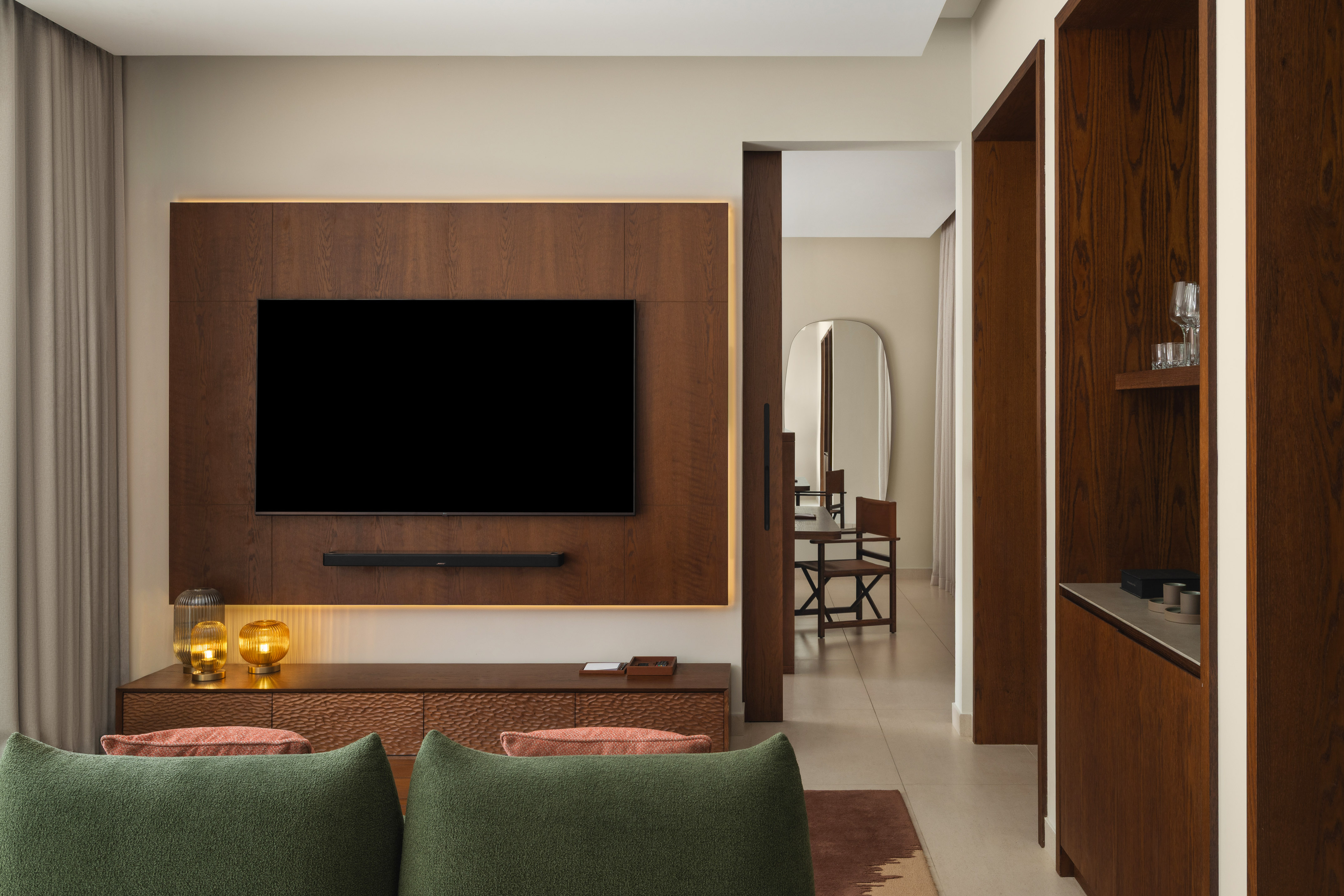 Modern living room with TV on wood panel, media console, and green sofa.