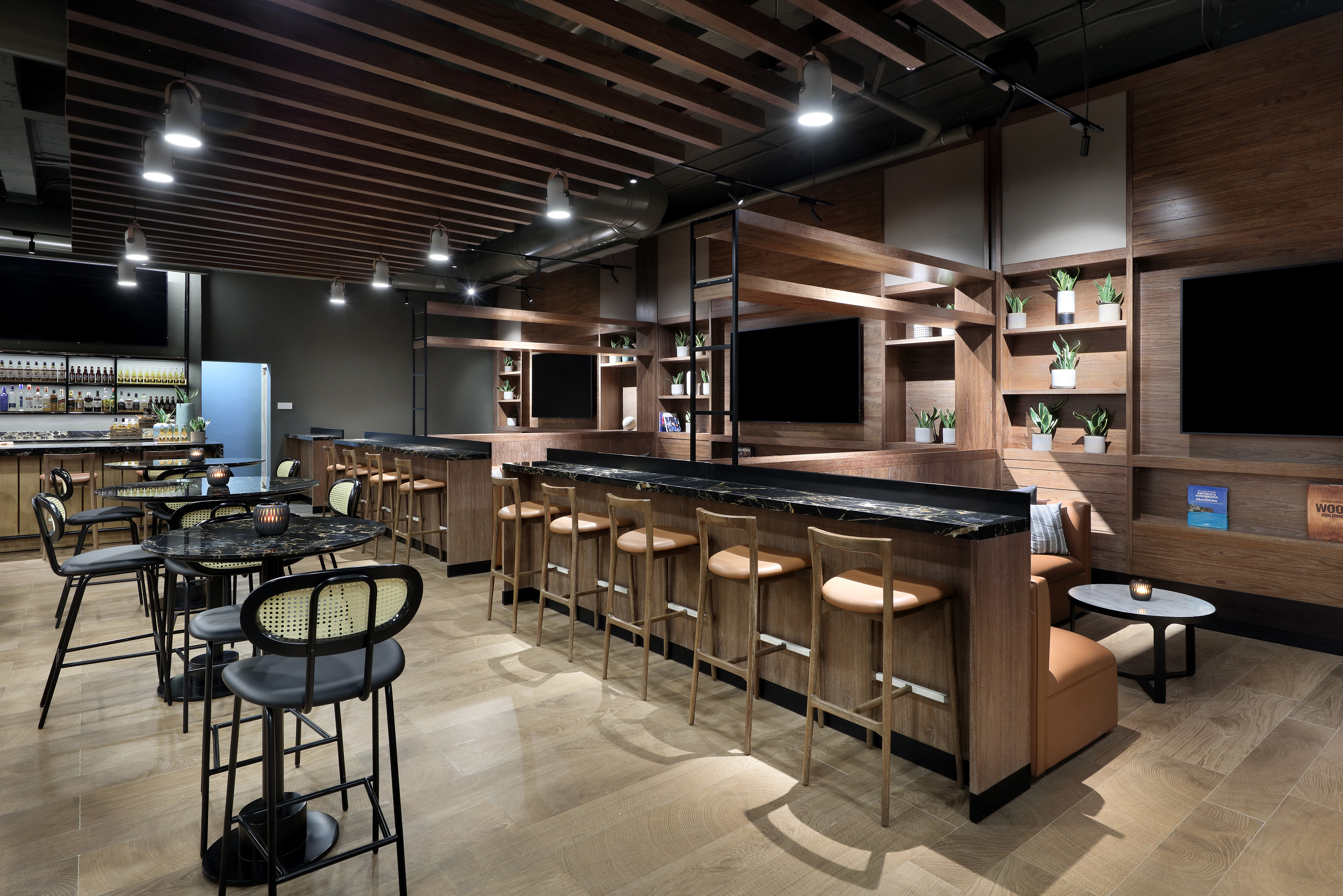Modern lounge bar with wood and marble design, diverse seating, and screens.