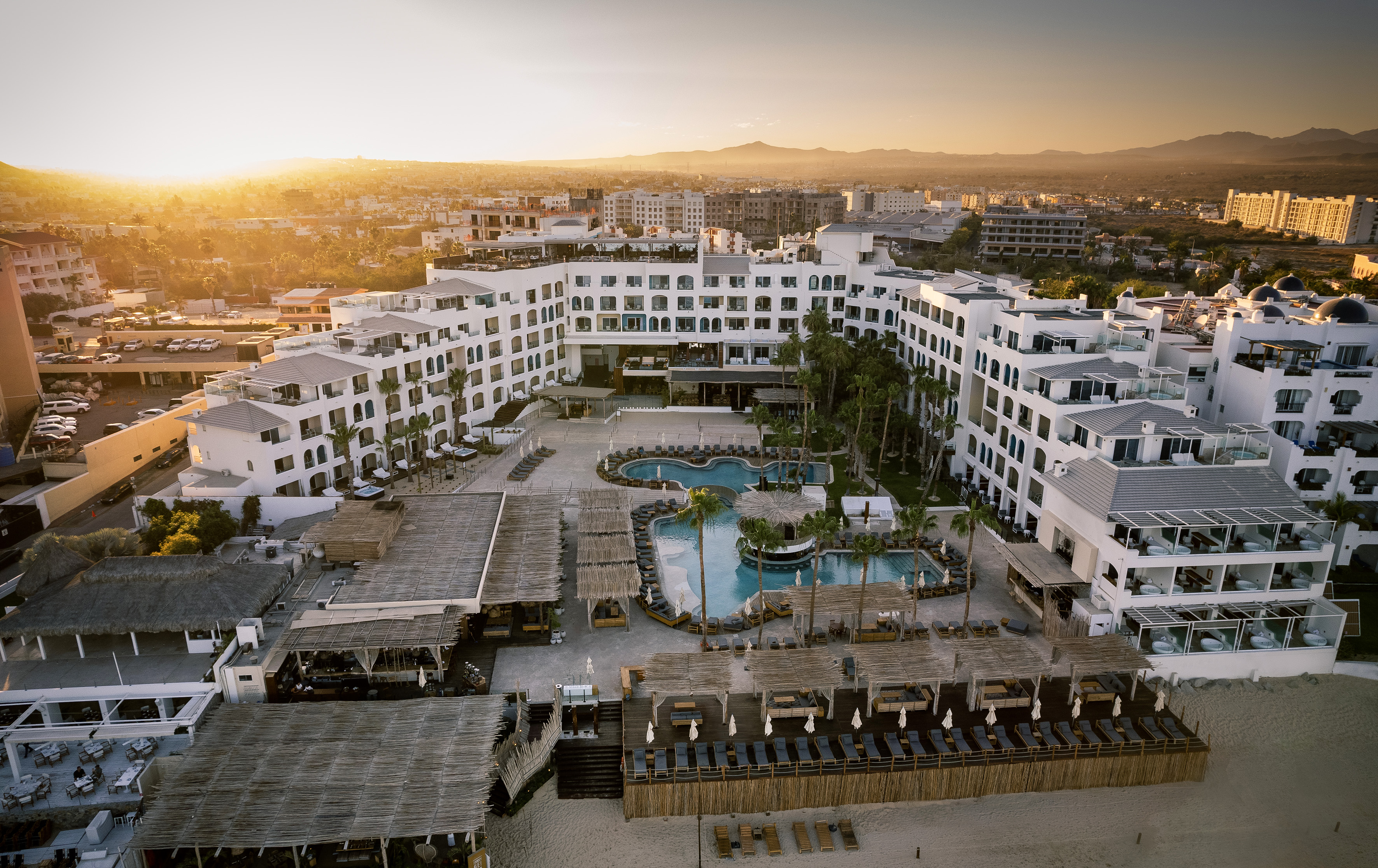 Luxury beachfront resort with pools and white buildings, aerial sunset view.