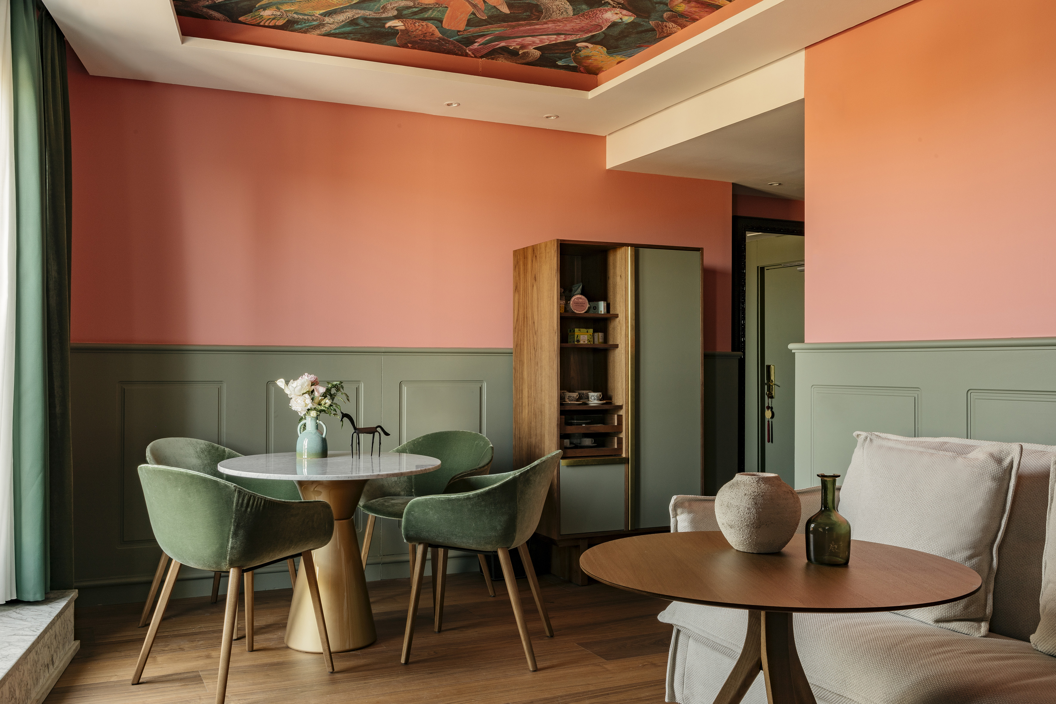 Colorful dining area with peach walls, green chairs, marble table, and bird ceiling.