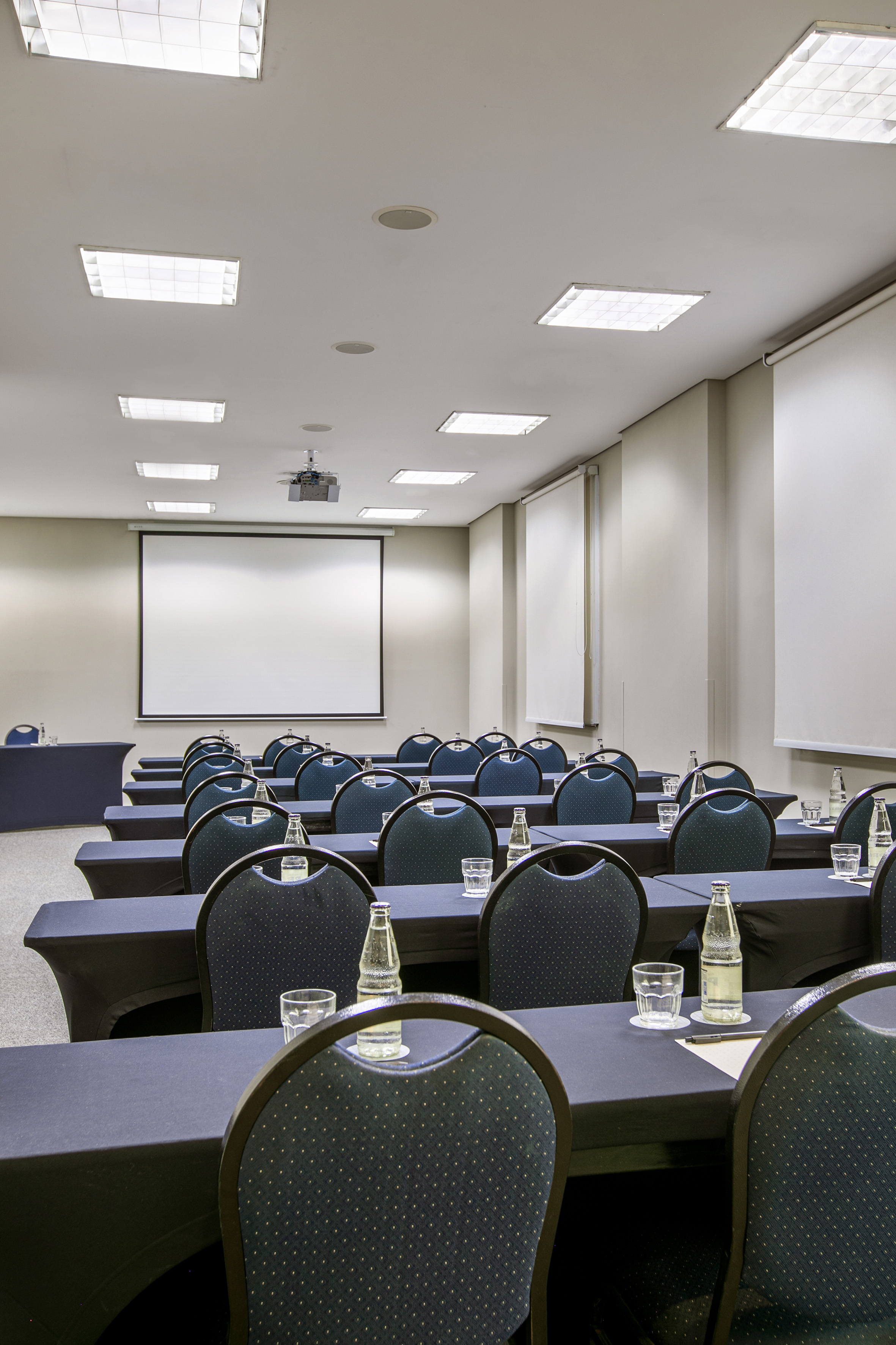 Meeting room with projector screen, dark tables, chairs, and bottled water.