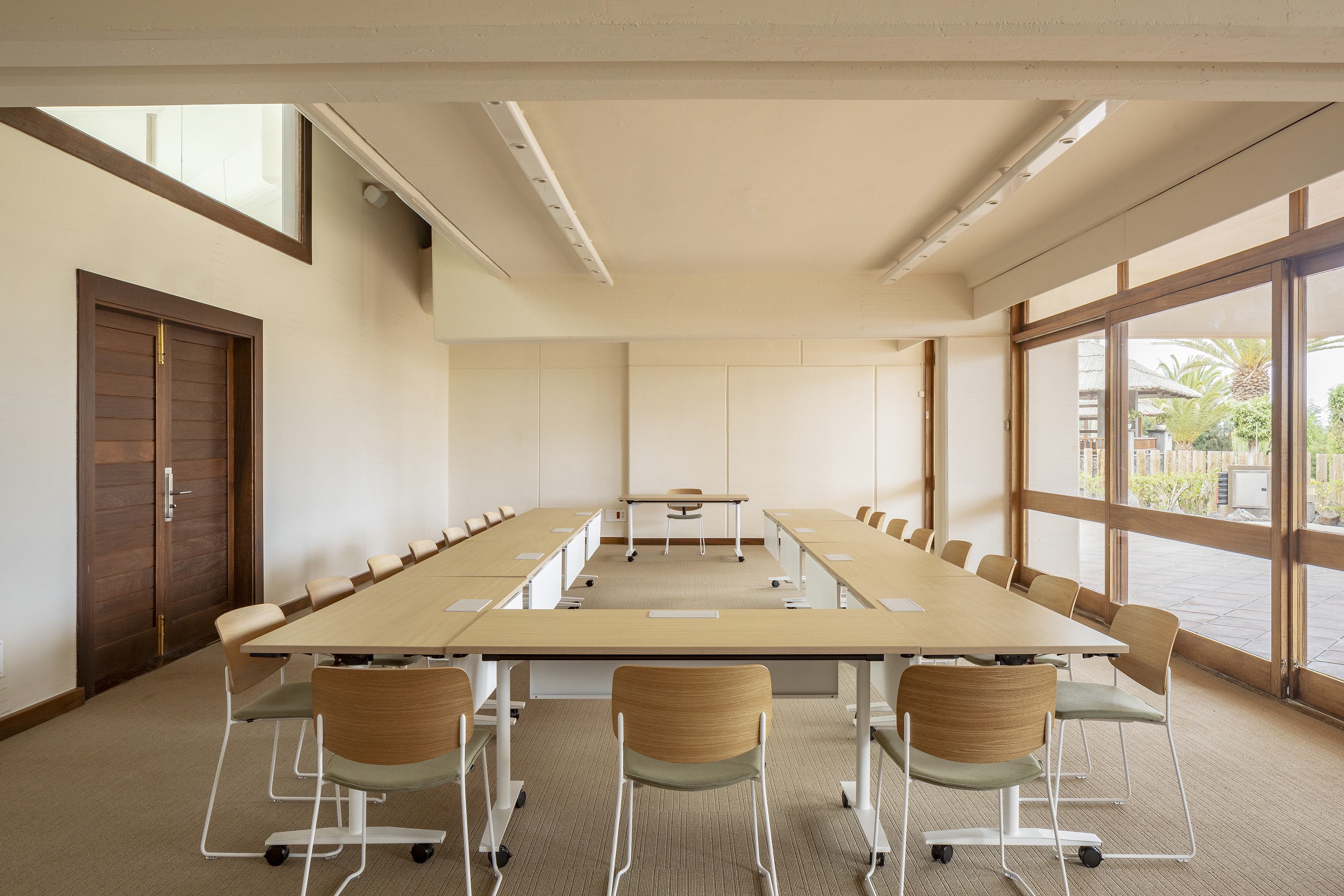 Modern U-shaped conference room with natural light, wood table, and green chairs.