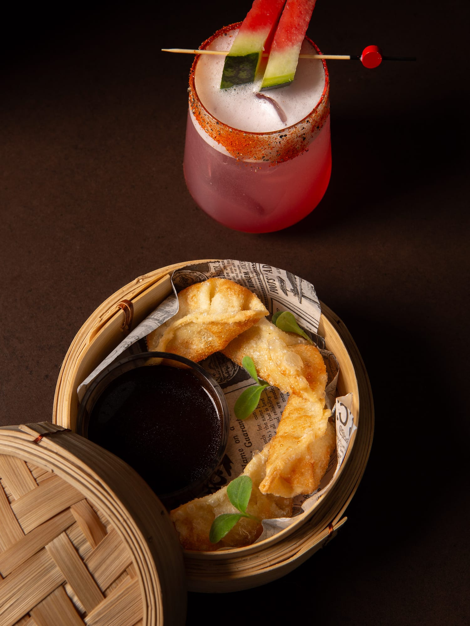 Watermelon cocktail with spicy rim and fried dumplings in bamboo steamer.