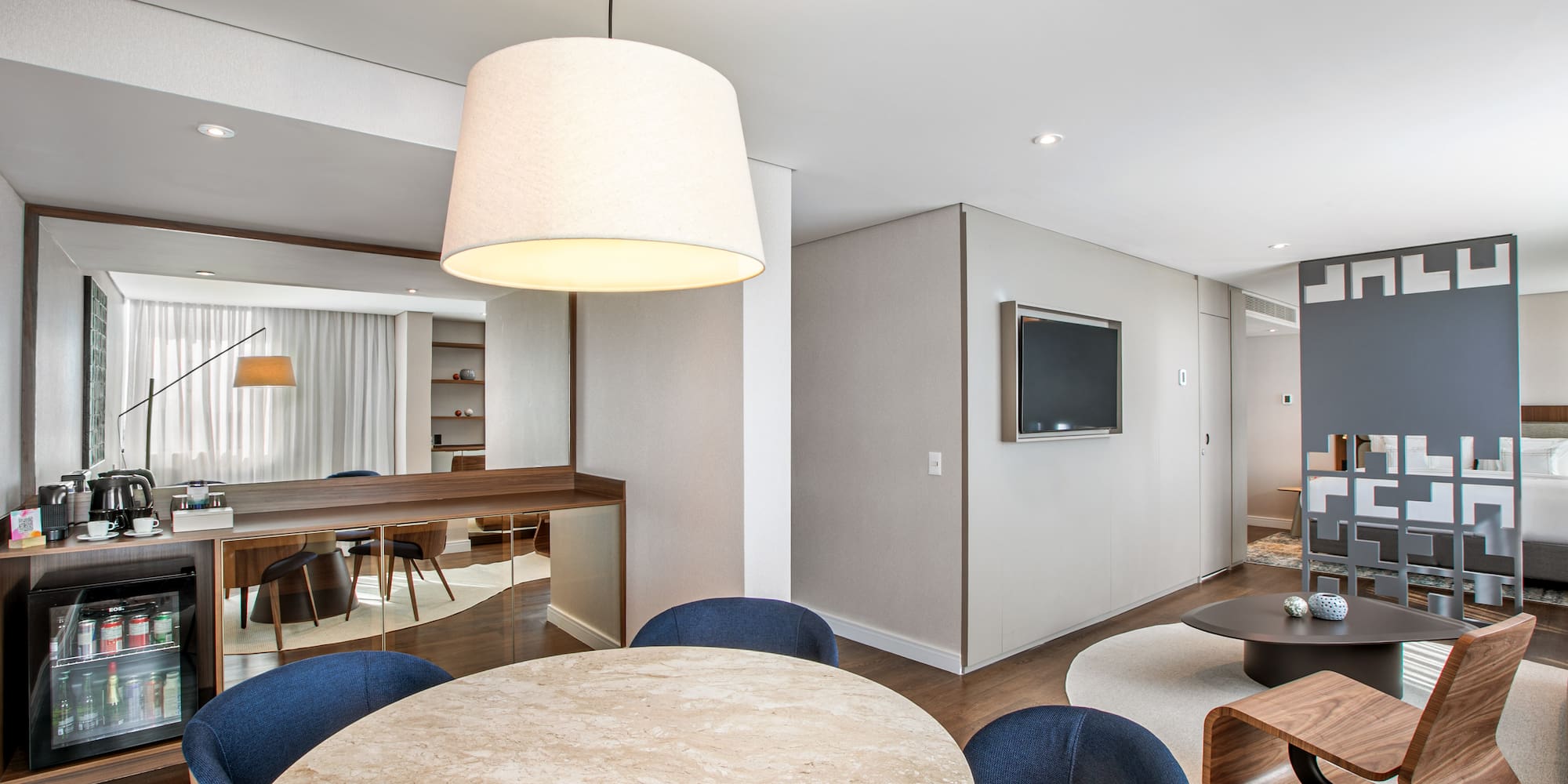 Modern hotel suite with dining area, mini-bar, and contemporary living room.