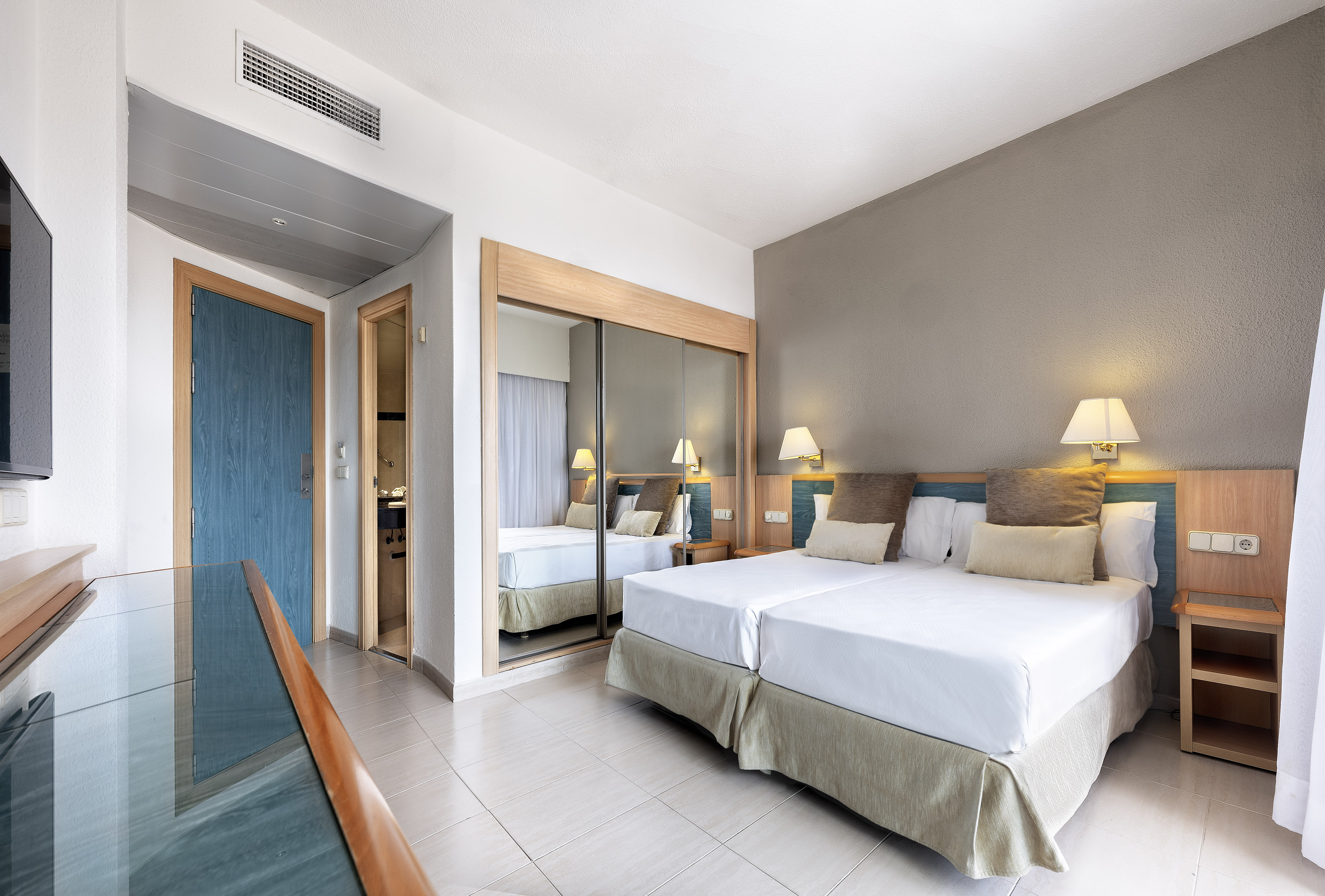 Hotel room with twin beds, mirrored wardrobe, blue door, and tiled floor.