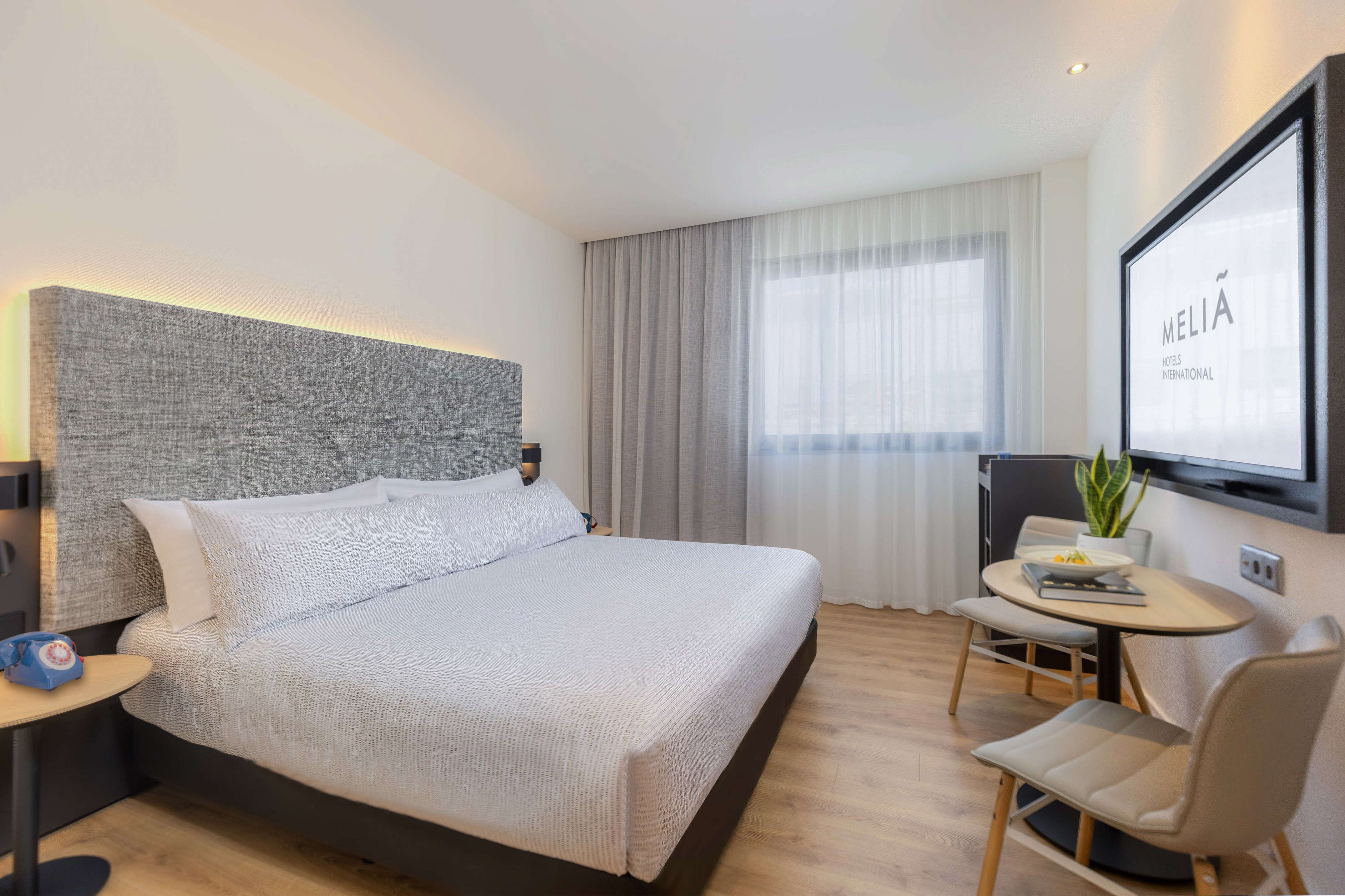 Meliá Hotels modern guest room with bed, TV, workspace, and bright window.