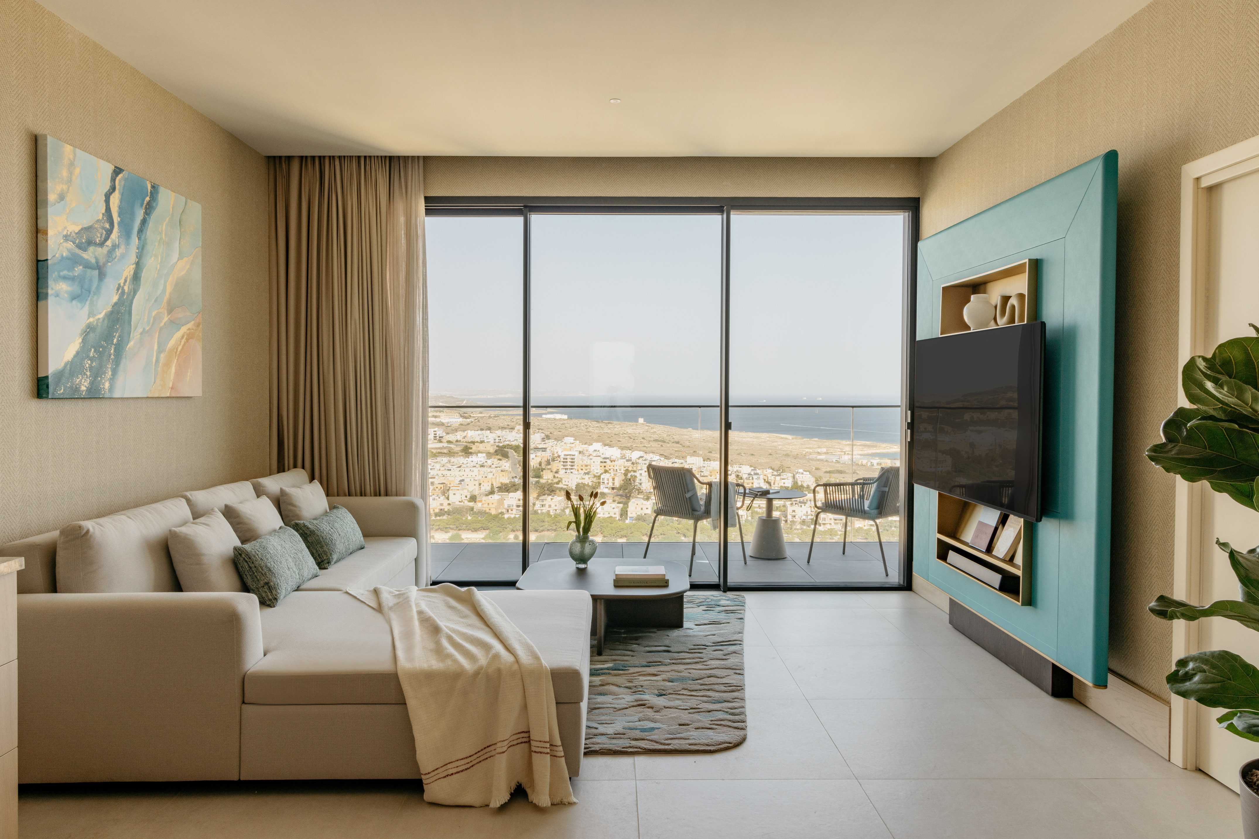 Modern living room with beige sofa, ocean view balcony, and teal TV unit.