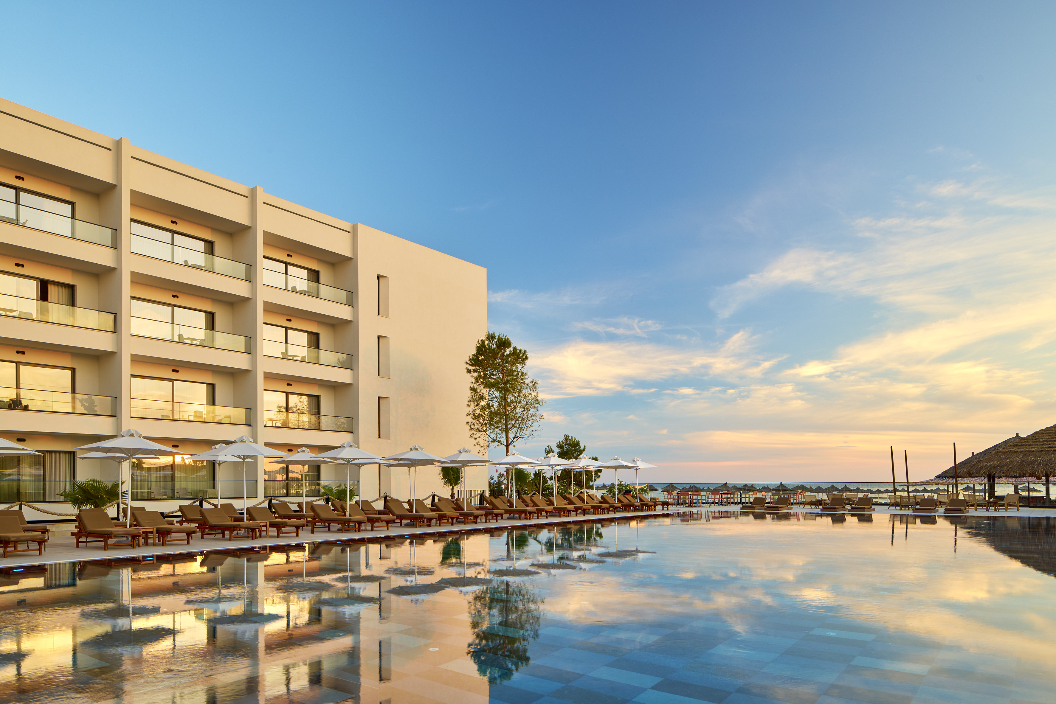Modern resort hotel with large pool, sun loungers, and sunset reflections.