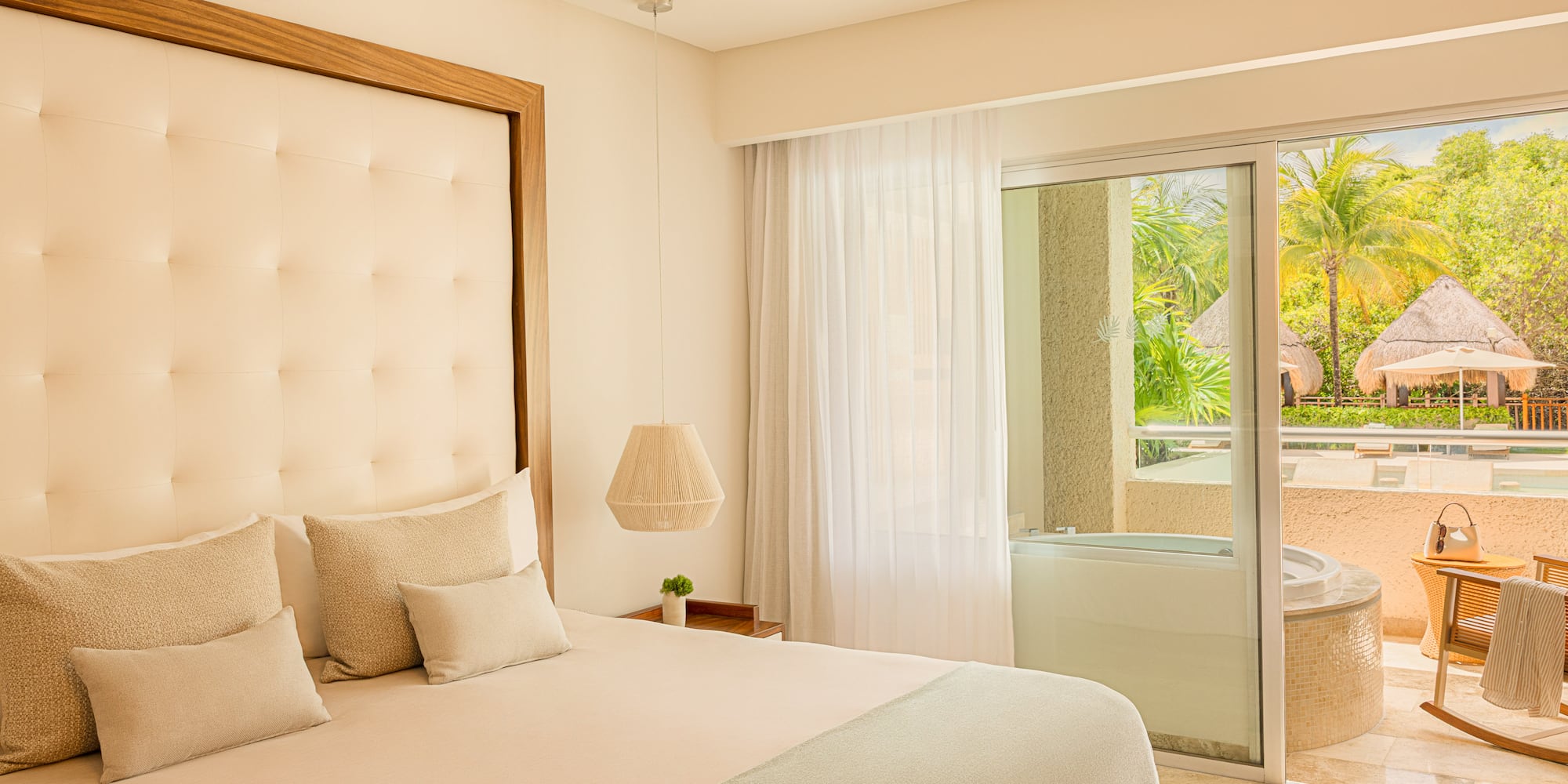 Bright hotel bedroom with king bed, balcony hot tub, and tropical garden view.