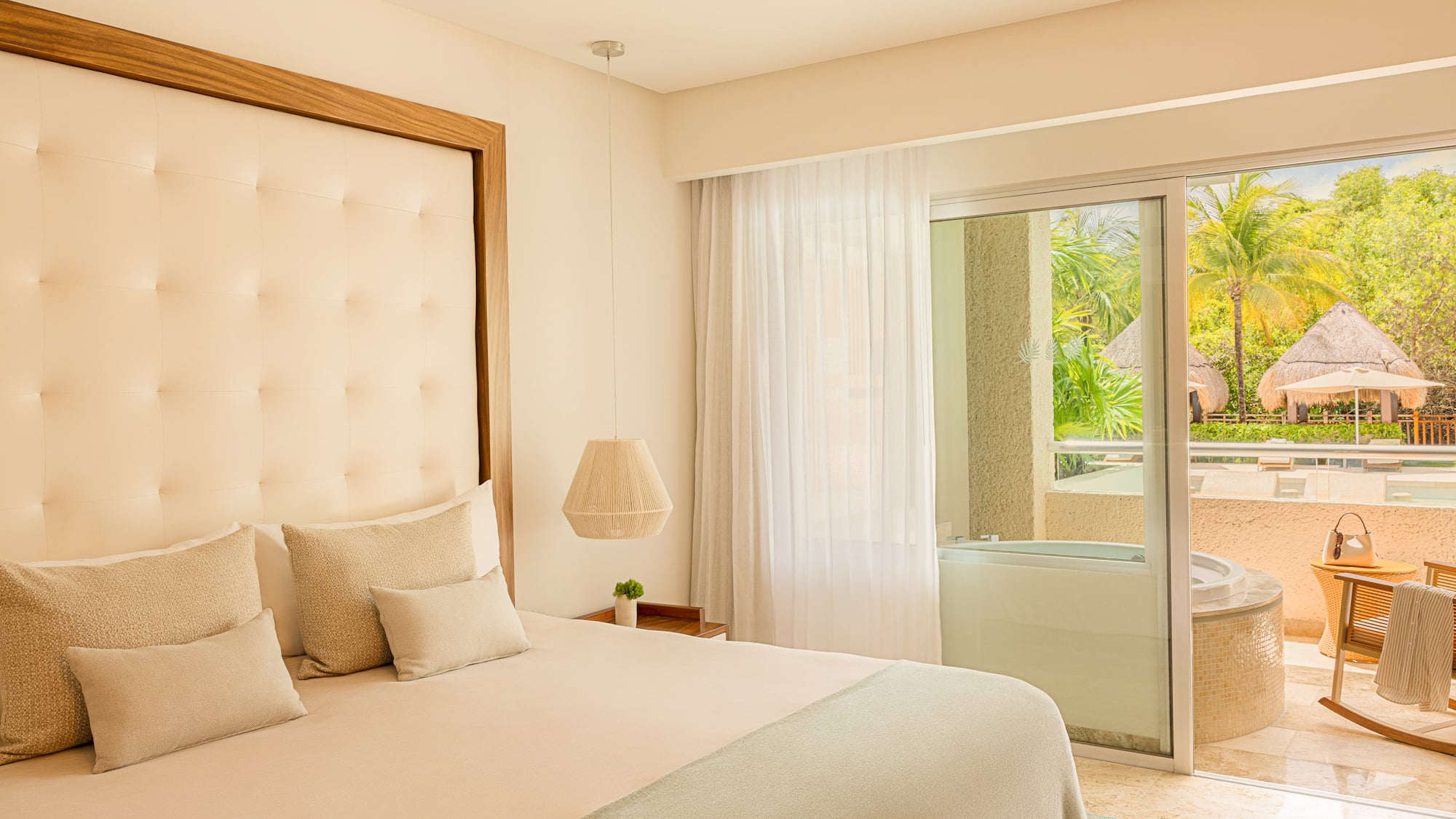 Bright hotel bedroom with king bed, balcony hot tub, and tropical garden view.