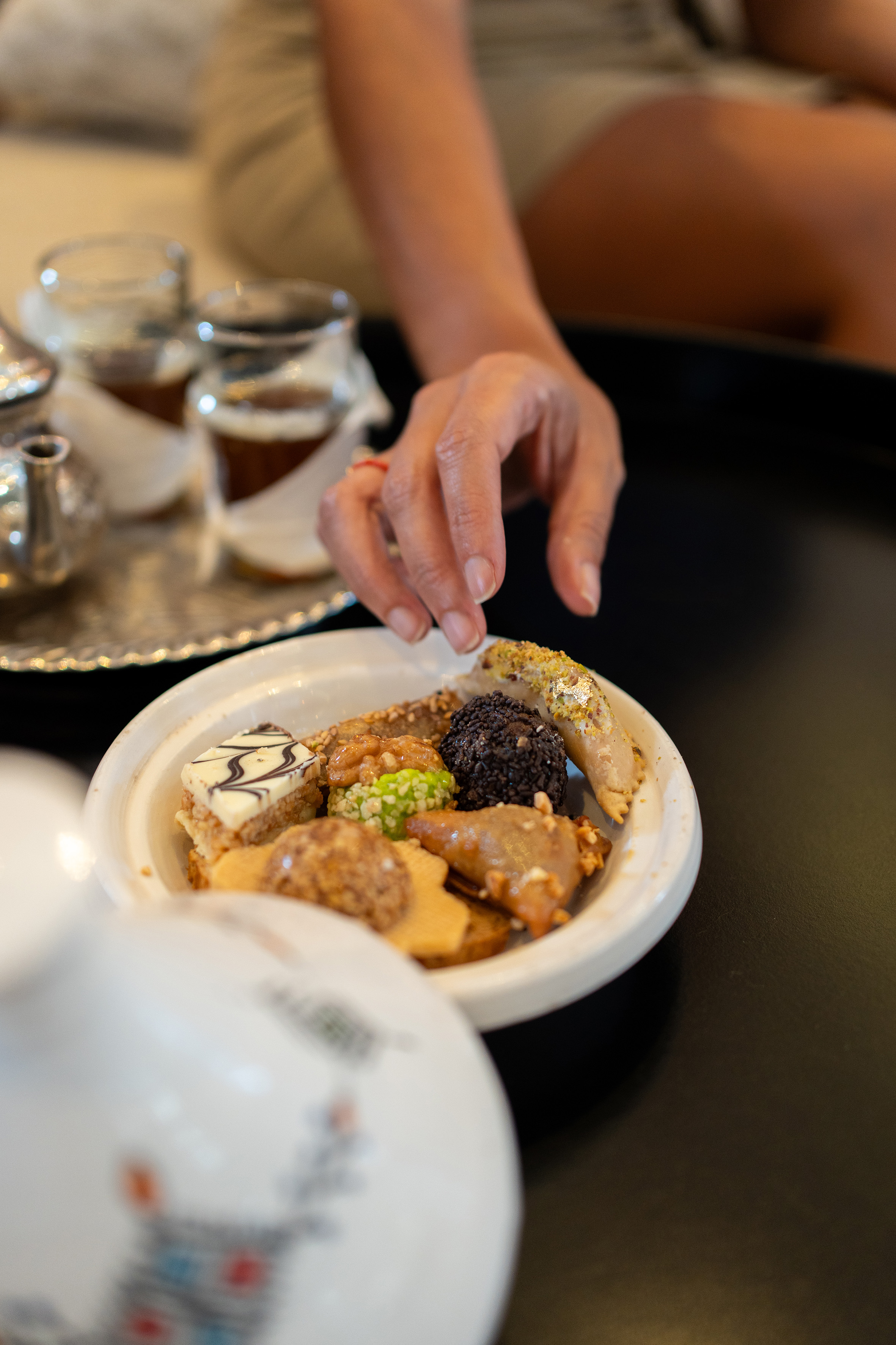 Hand selecting Moroccan pastries from a white plate, with tea service nearby.
