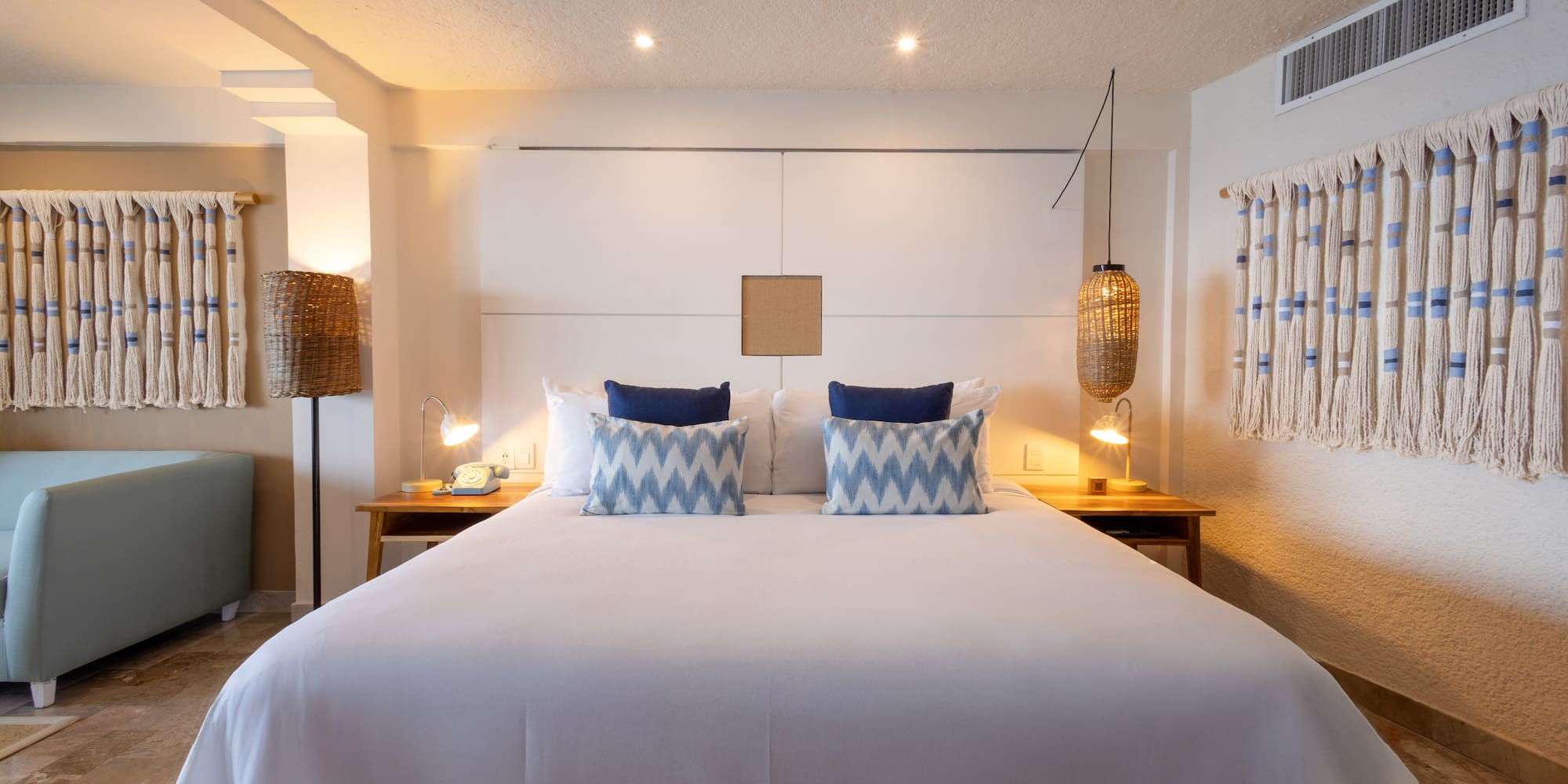 Hotel bedroom with king bed, blue accent pillows, and natural woven decor.