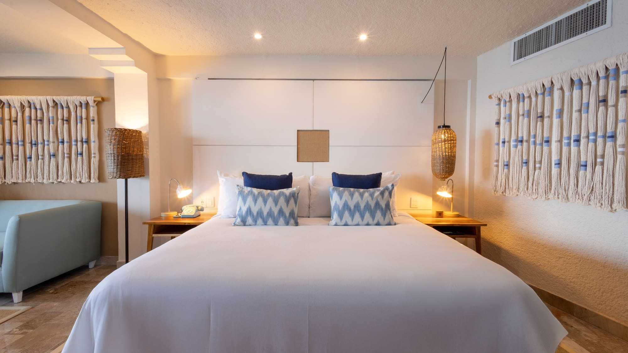 Hotel bedroom with king bed, blue accent pillows, and natural woven decor.