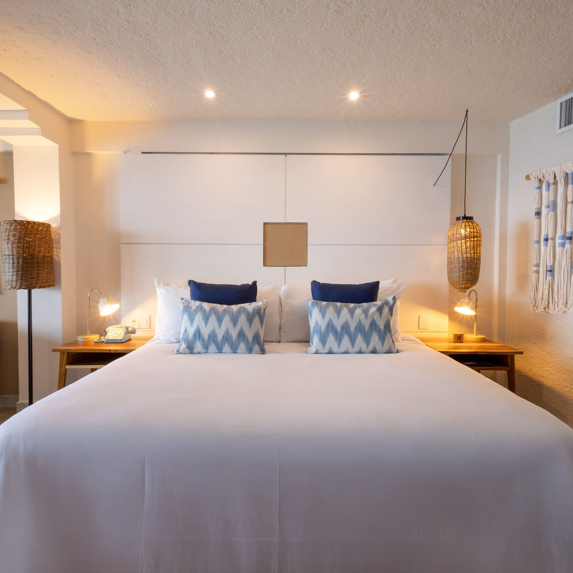 Hotel bedroom with king bed, blue accent pillows, and natural woven decor.