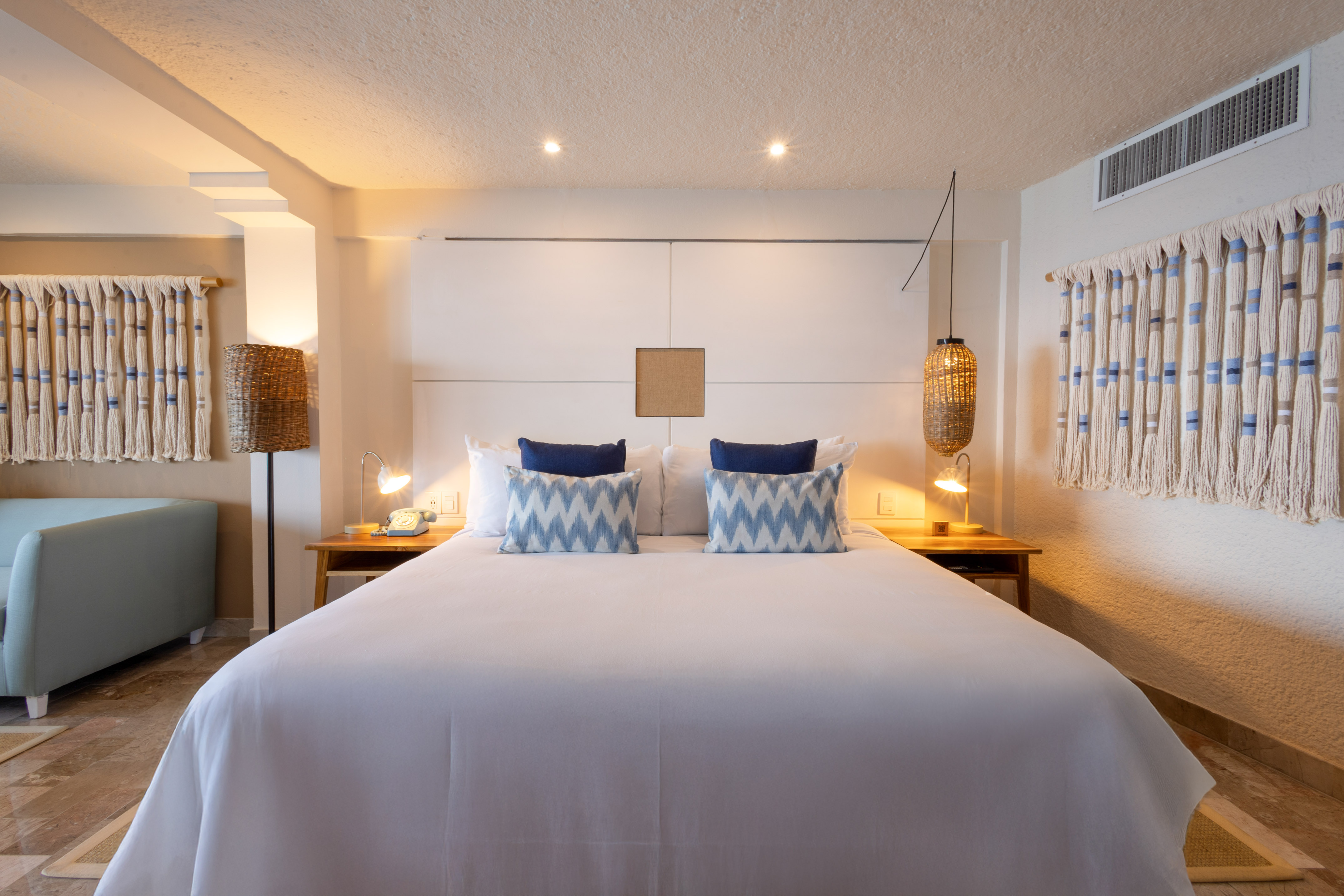 Hotel bedroom with king bed, blue accent pillows, and natural woven decor.