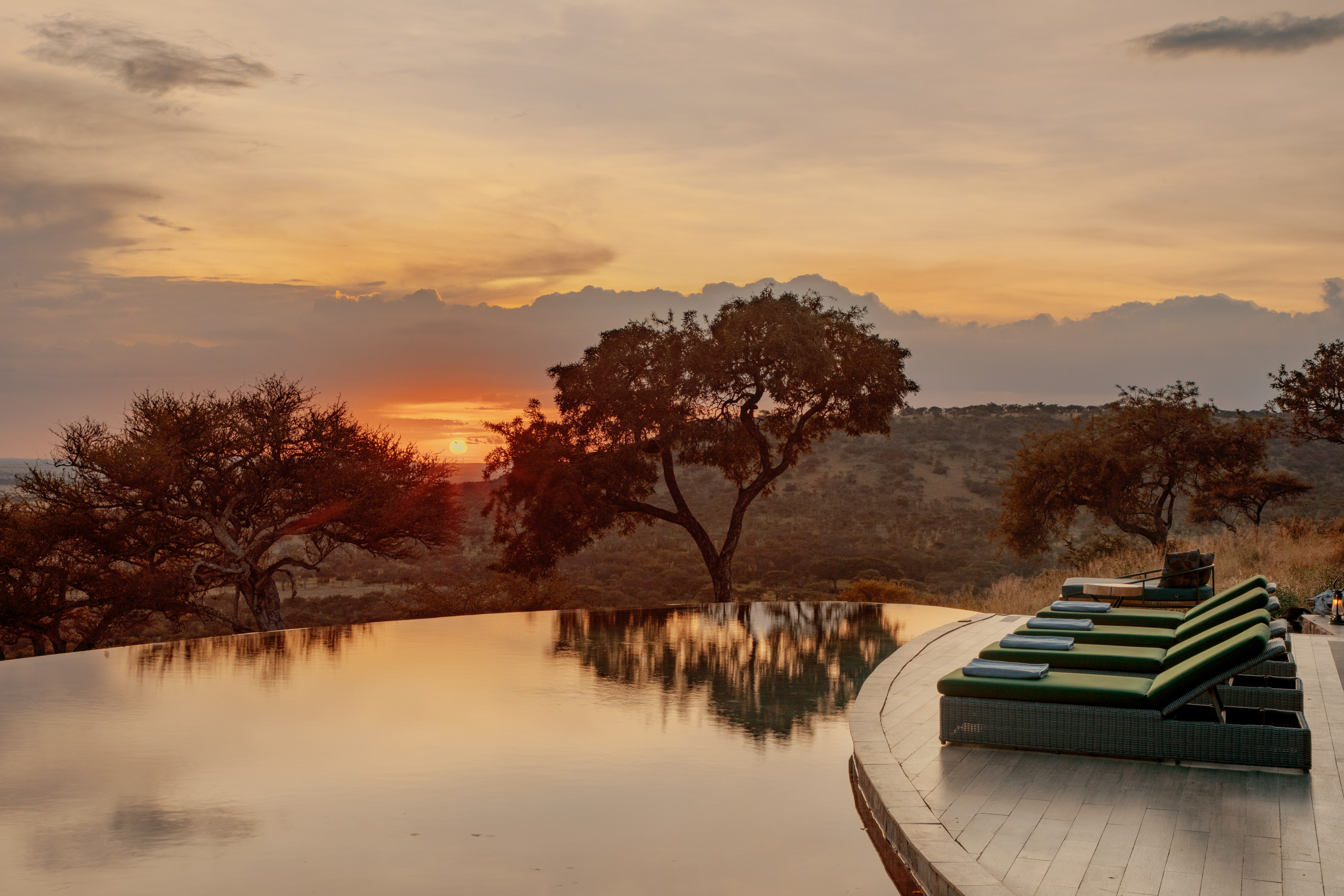African savanna sunset reflecting in infinity pool with resort lounge chairs.