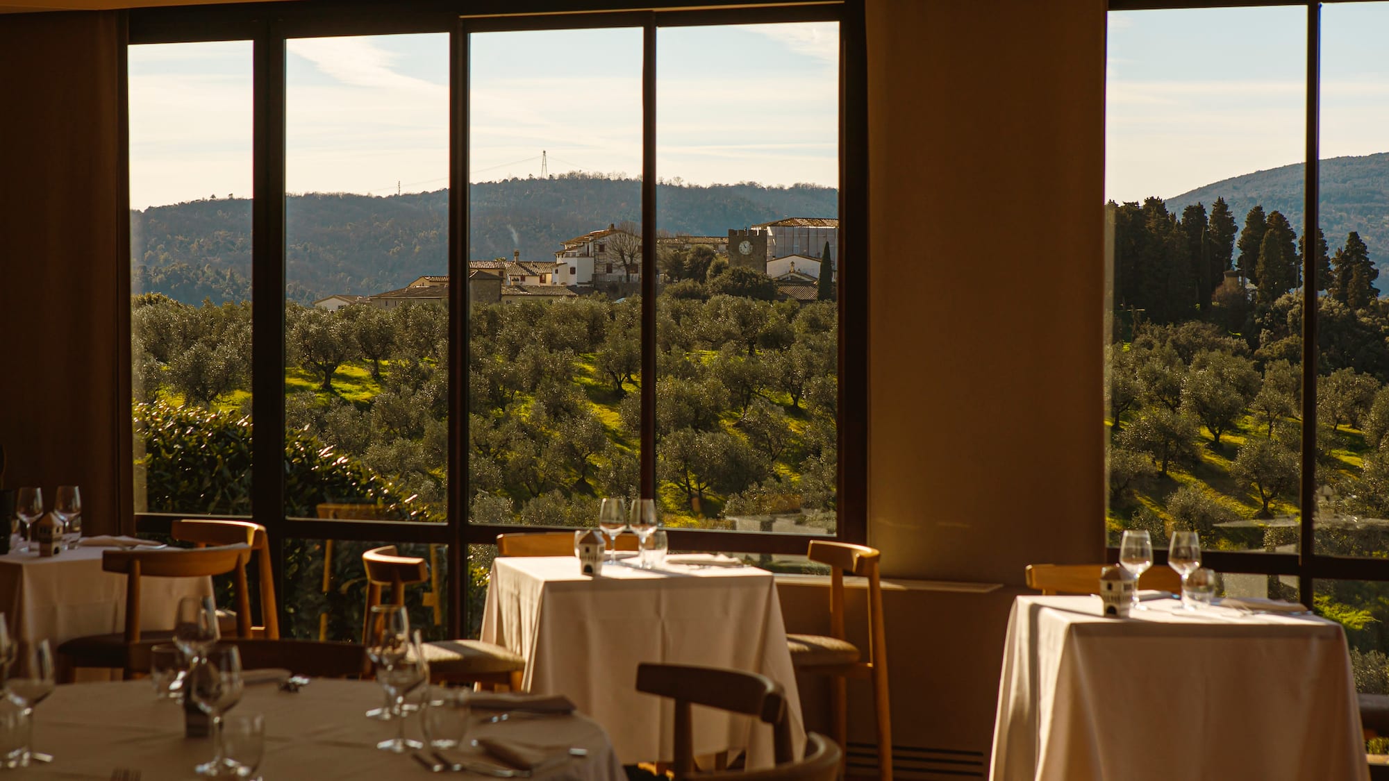 a table set up with chairs and glasses in a room with trees and buildings