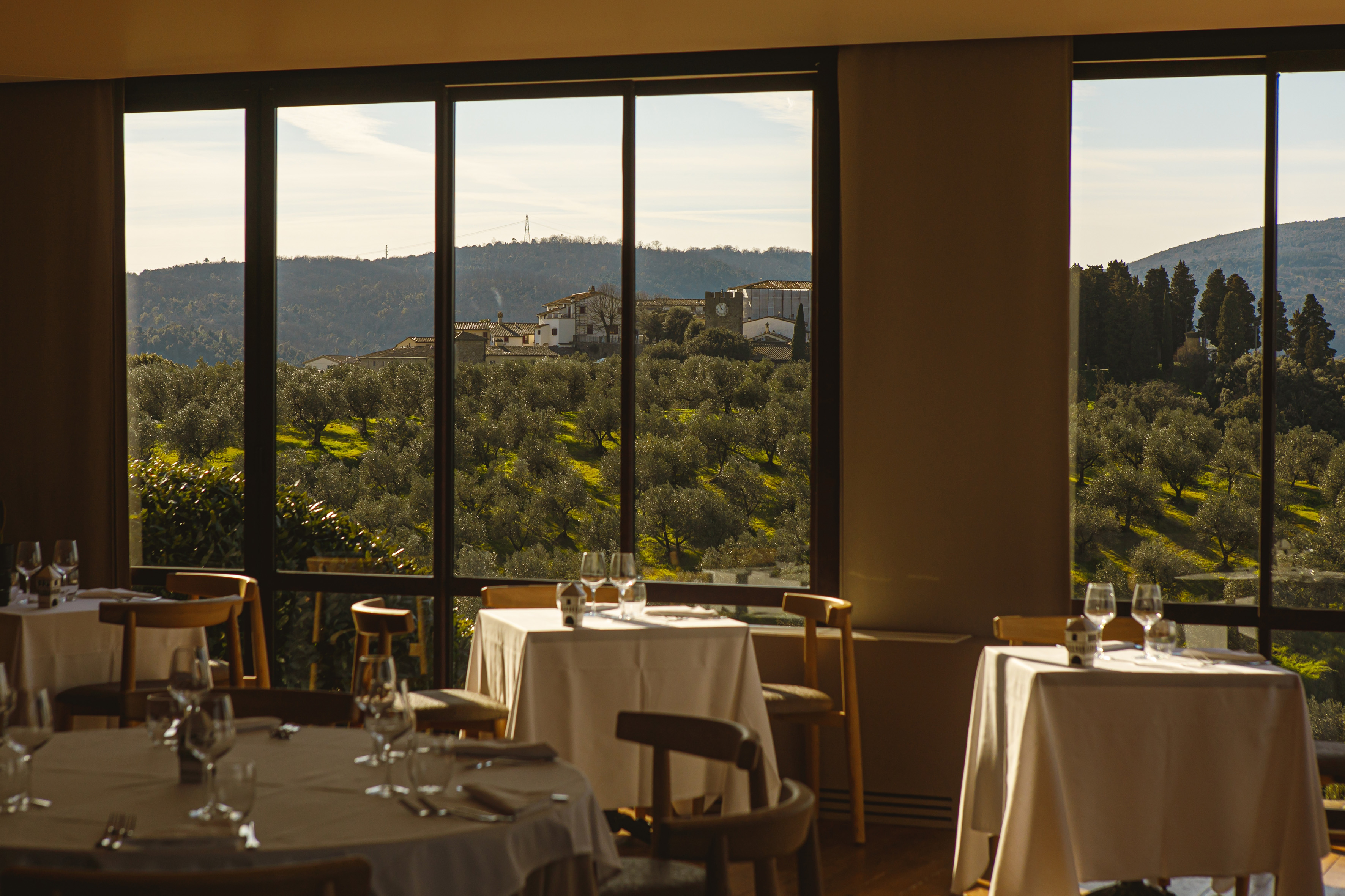 Restaurant dining room with panoramic view of Tuscan olive grove and village.