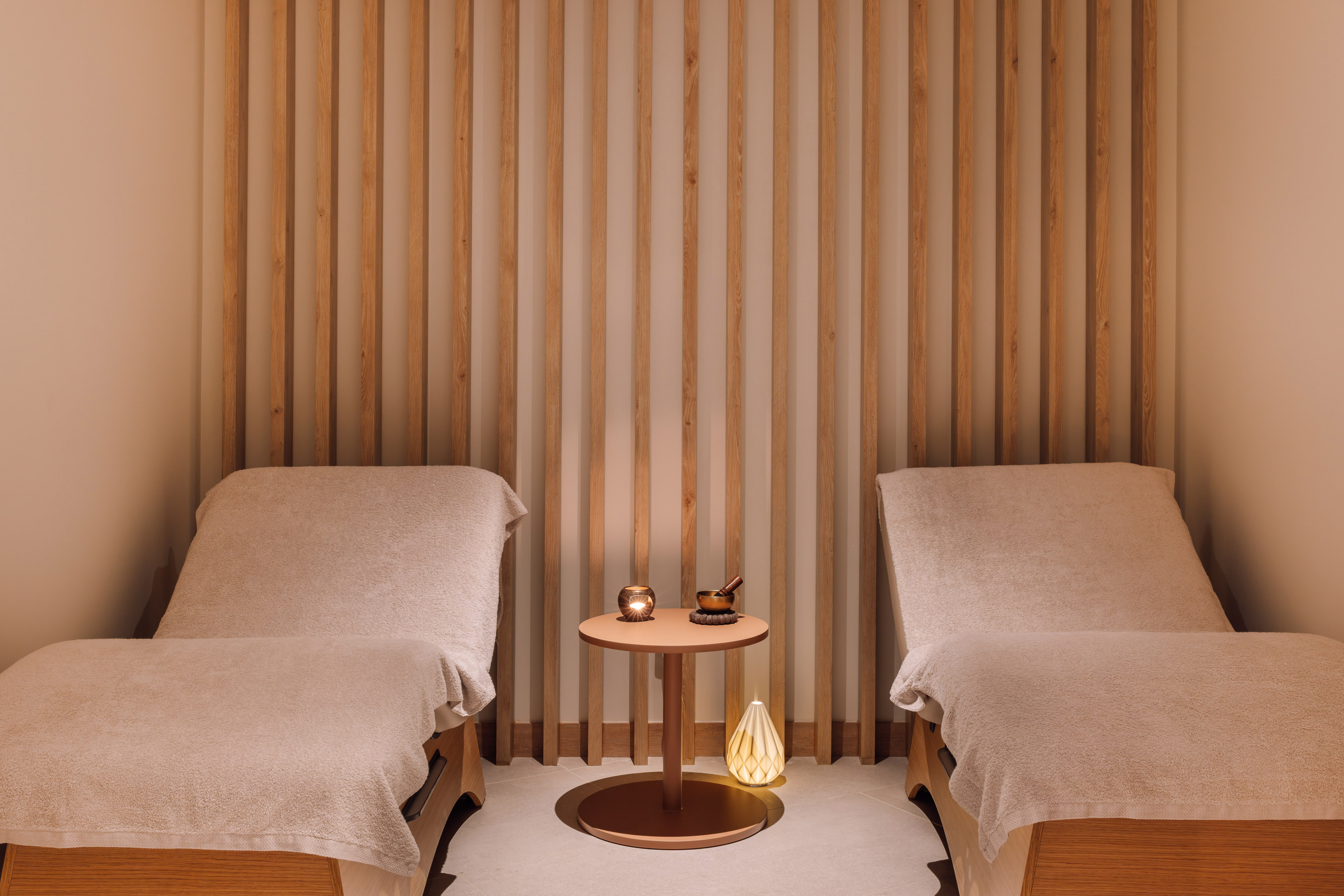 Serene spa room with two loungers, wood slat wall, ambient lighting.