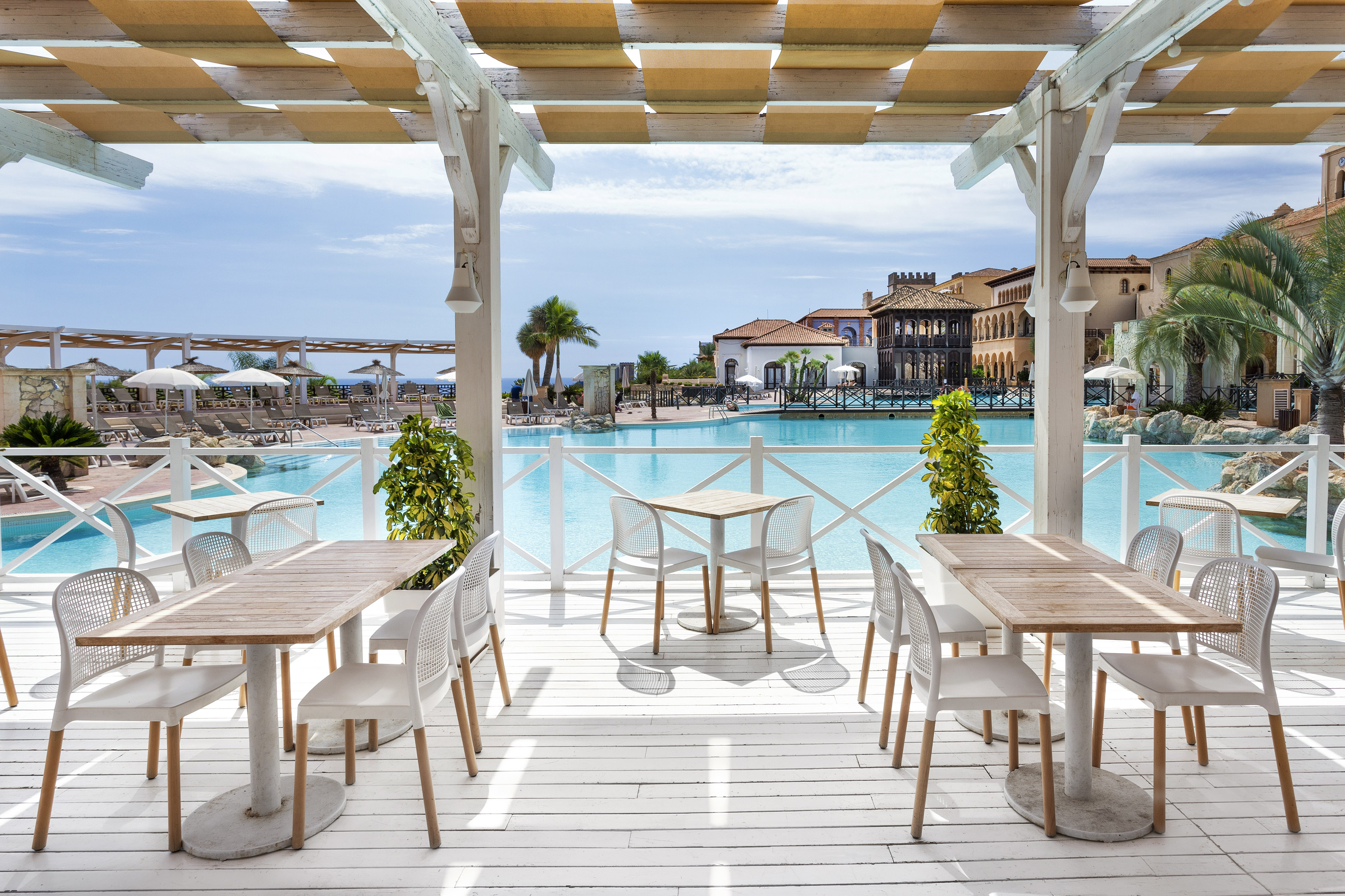 Poolside restaurant patio with tables, chairs, overlooking a luxury resort pool.