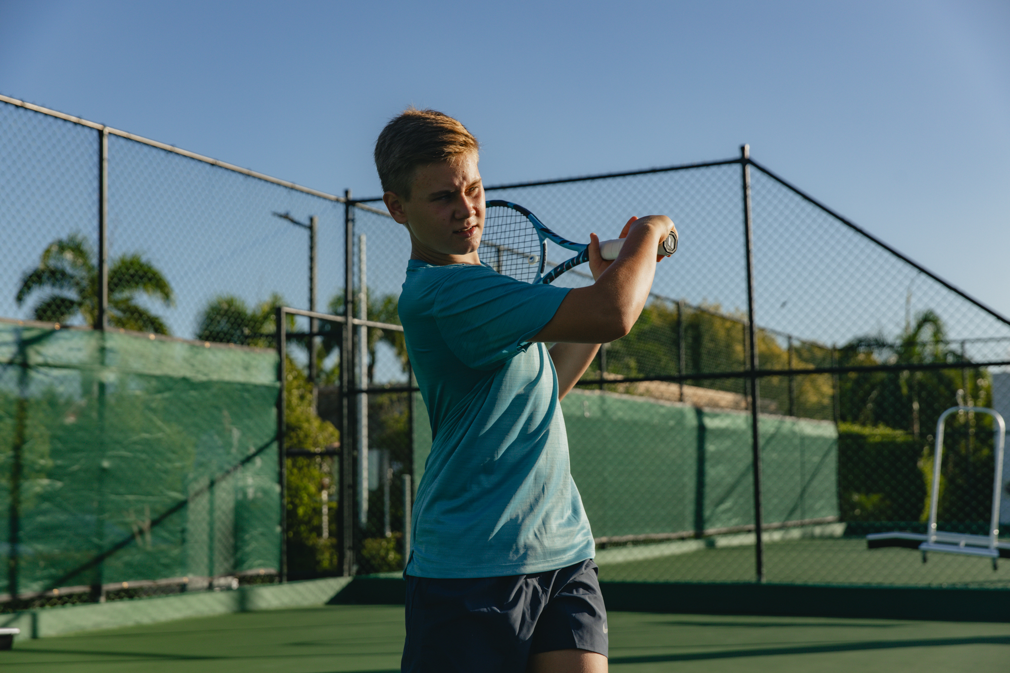Young male tennis player in blue shirt swinging racket on green court.