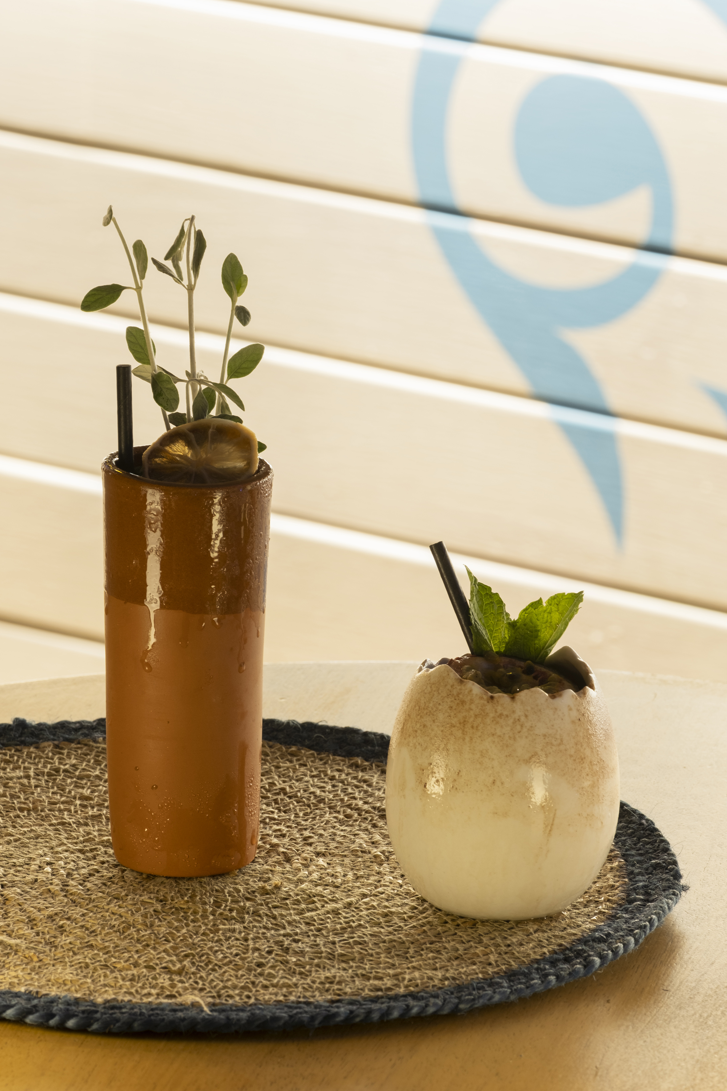 Refreshing cocktails in terracotta glass and eggshell cup with mint, on a woven mat.
