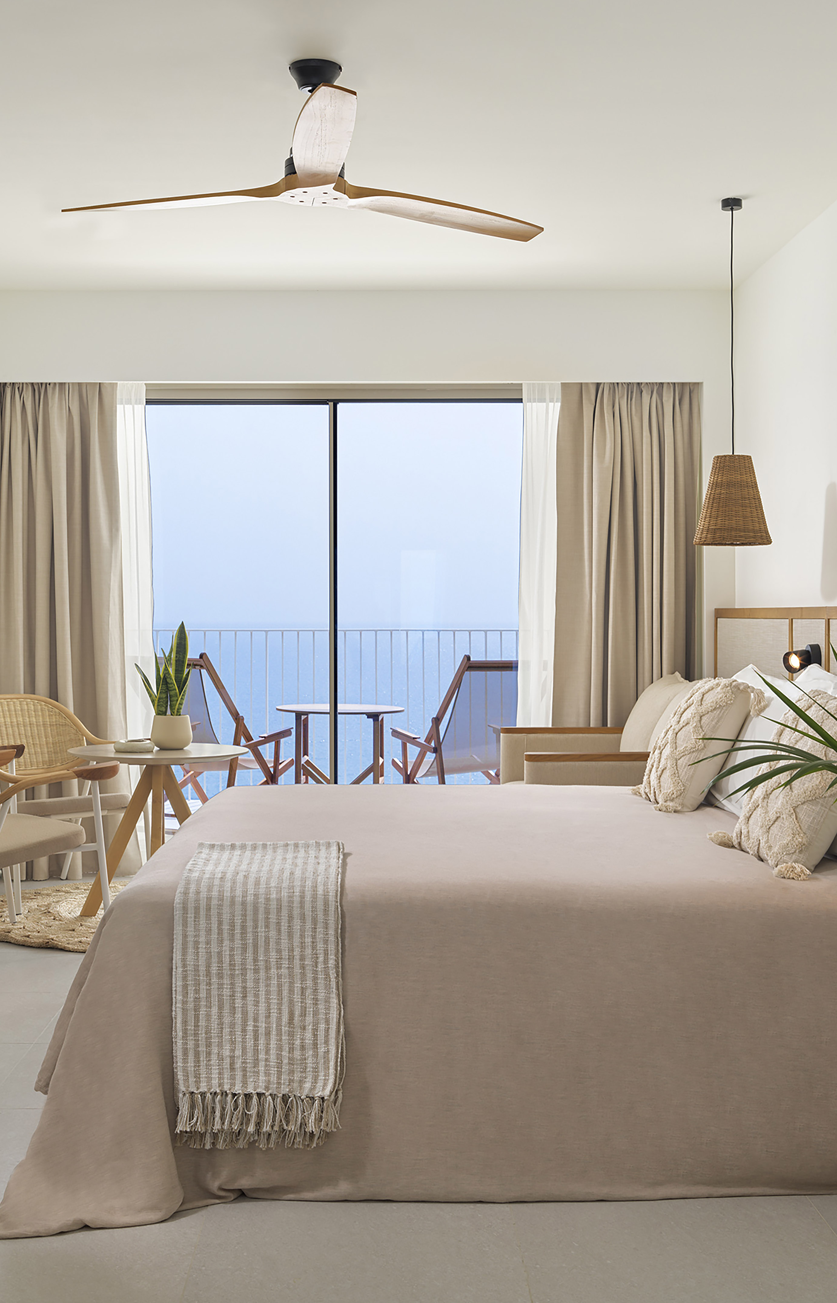 Bright bedroom with ocean view, balcony, neutral decor, and wooden ceiling fan.