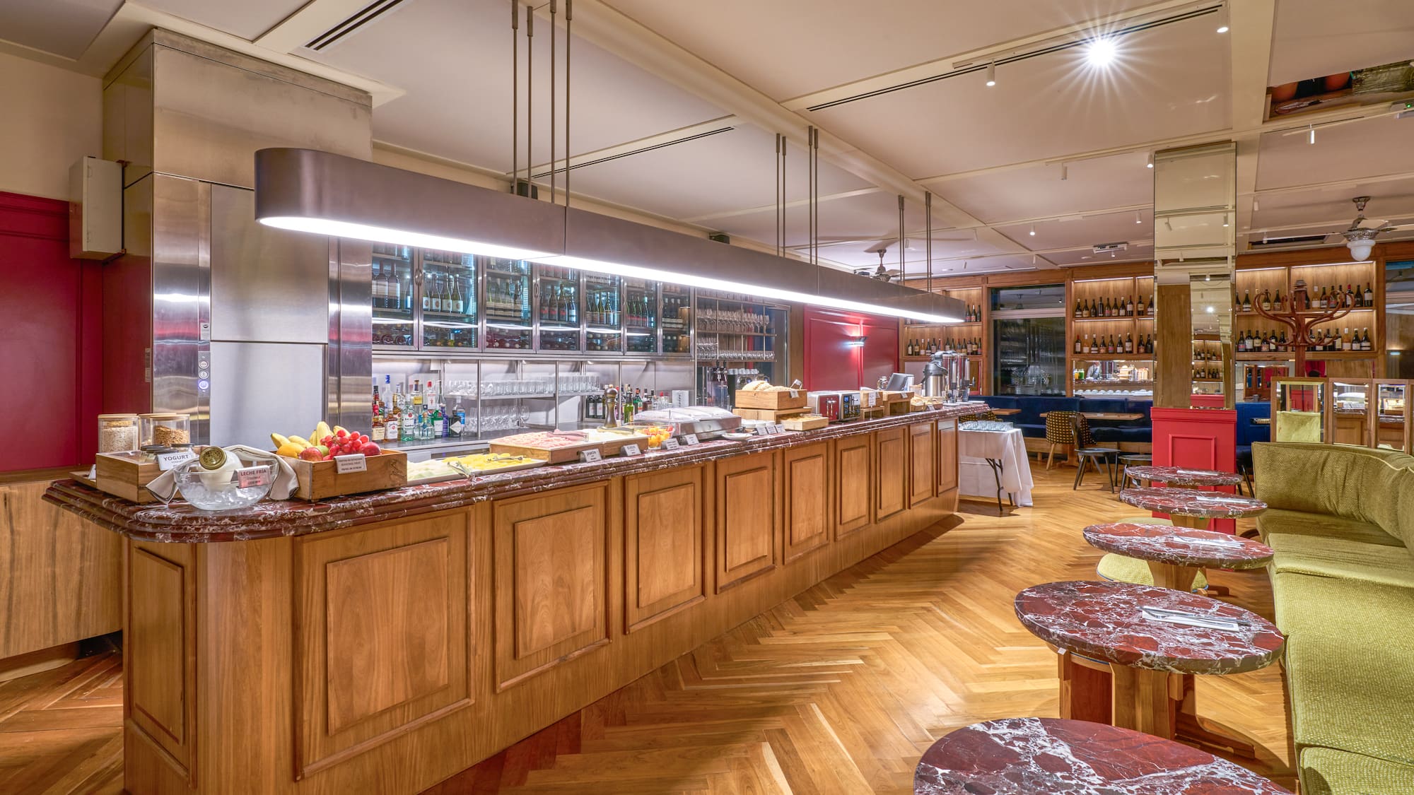 Modern hotel buffet bar with breakfast, wine display, and herringbone wood floor.