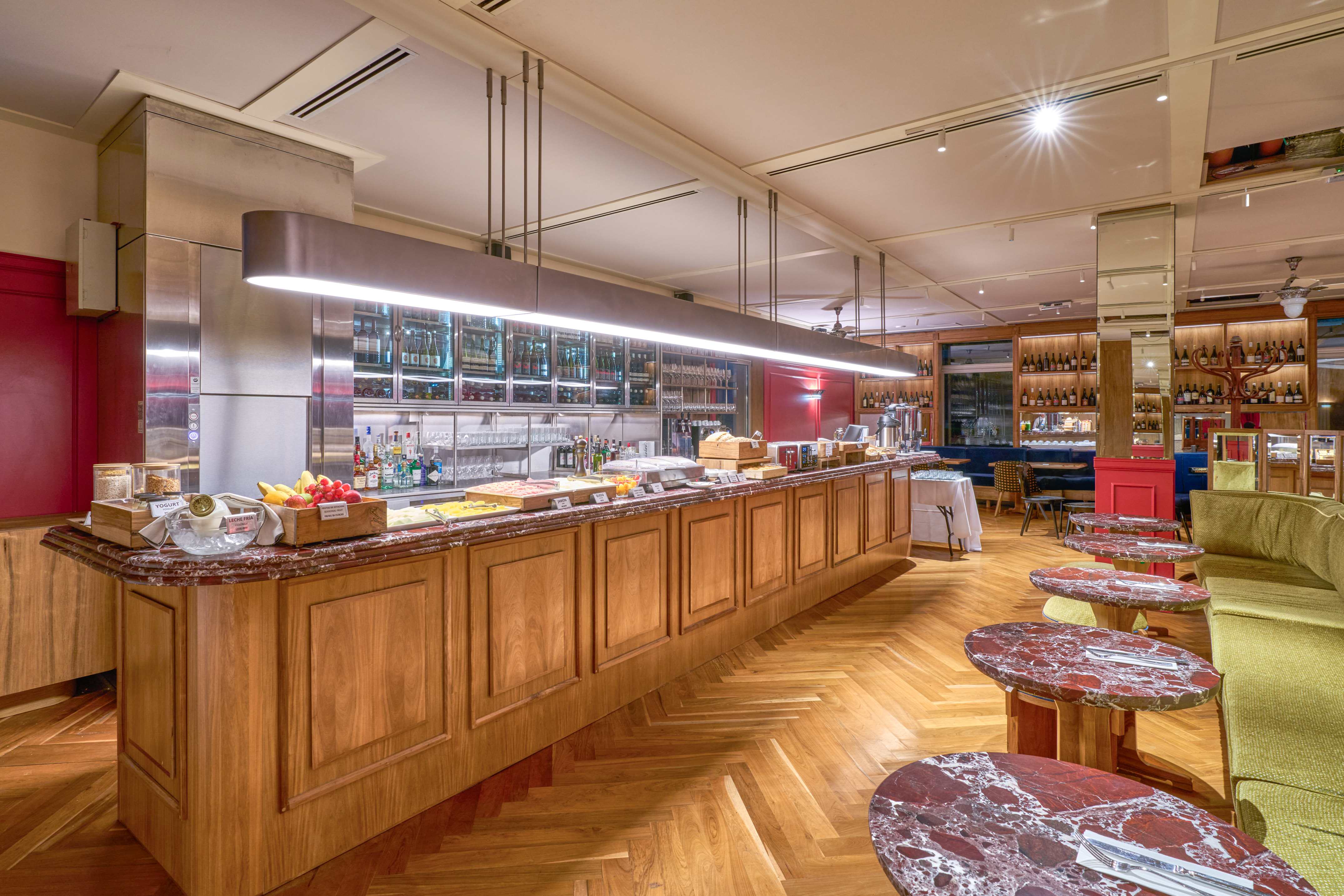 Modern hotel buffet bar with breakfast, wine display, and herringbone wood floor.