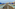 Blue thatched umbrellas, green sunbeds, and resort hotels on sandy beach.