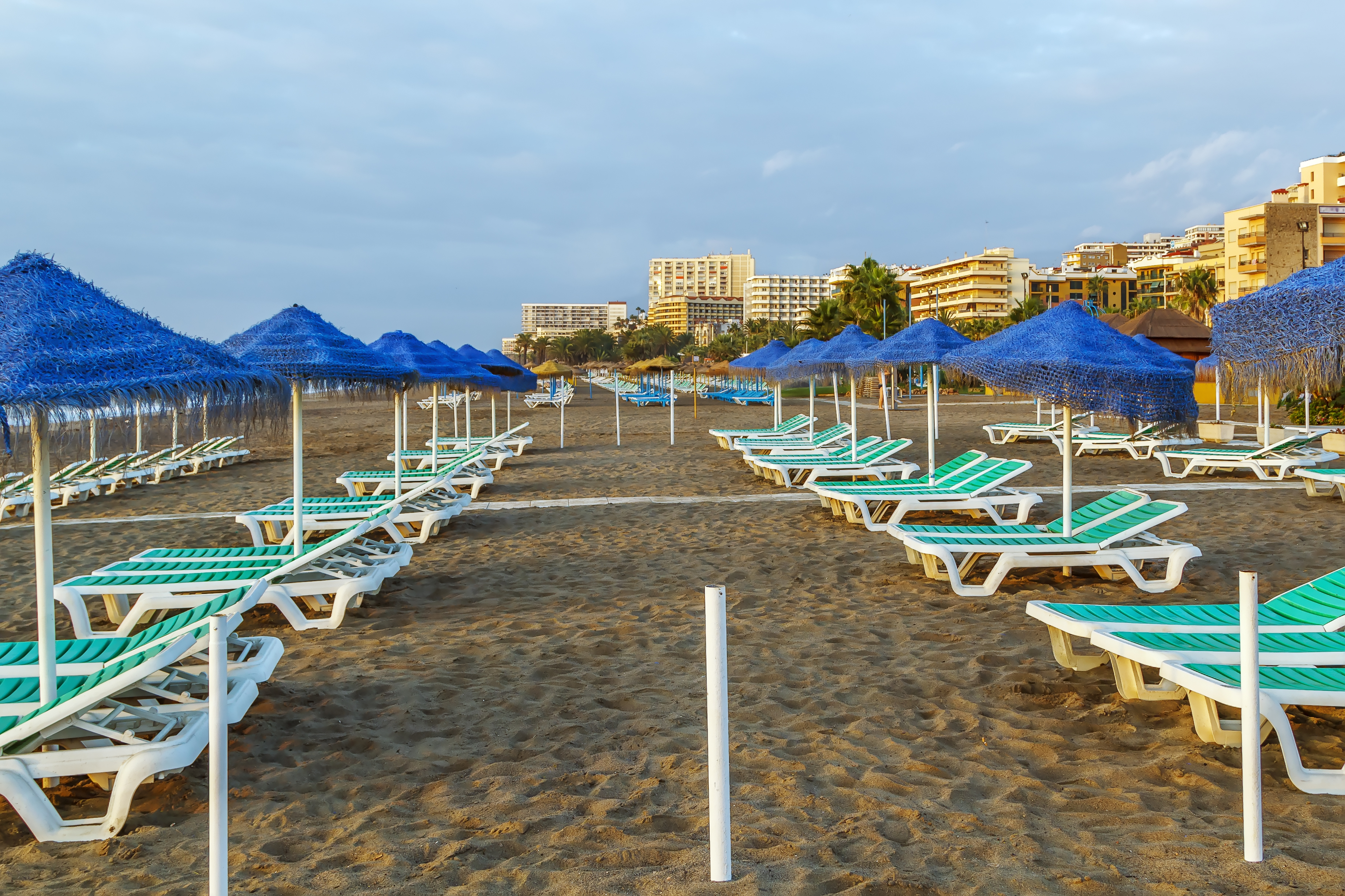 Blue thatched umbrellas, green sunbeds, and resort hotels on sandy beach.