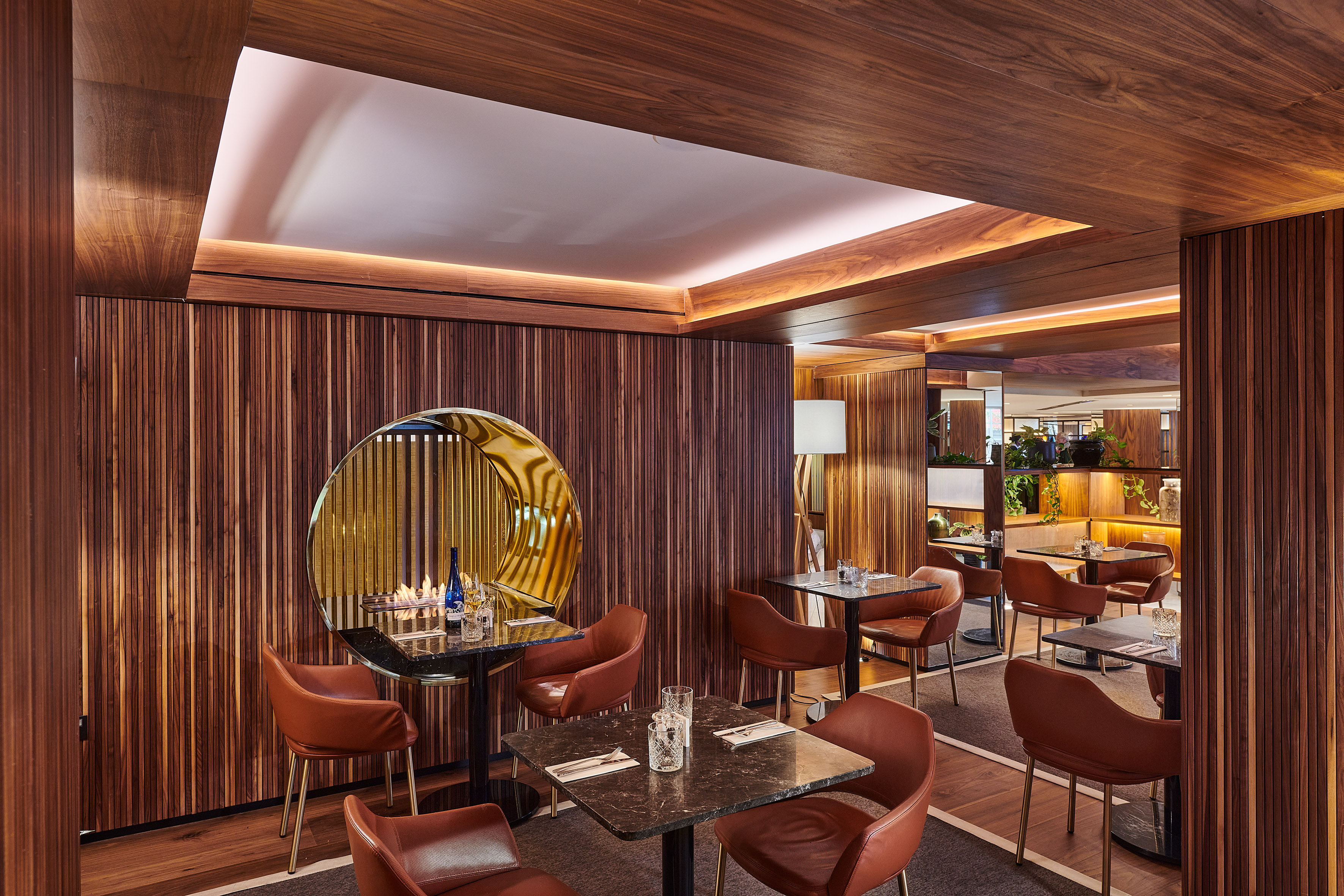 Restaurant with wood paneling, brown leather chairs, marble tables, and table fireplace.