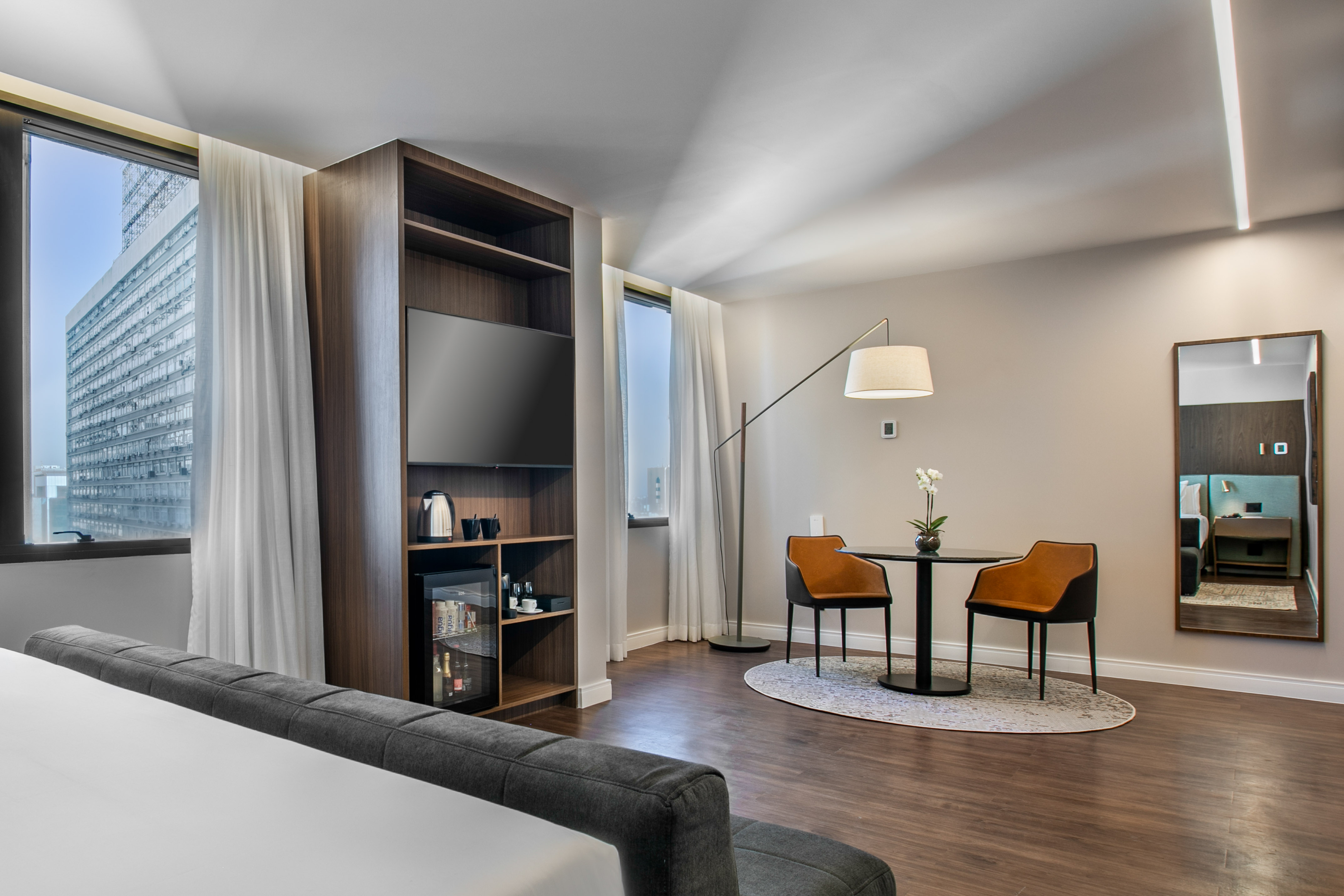 Modern hotel room with city view, entertainment console, and dining area.