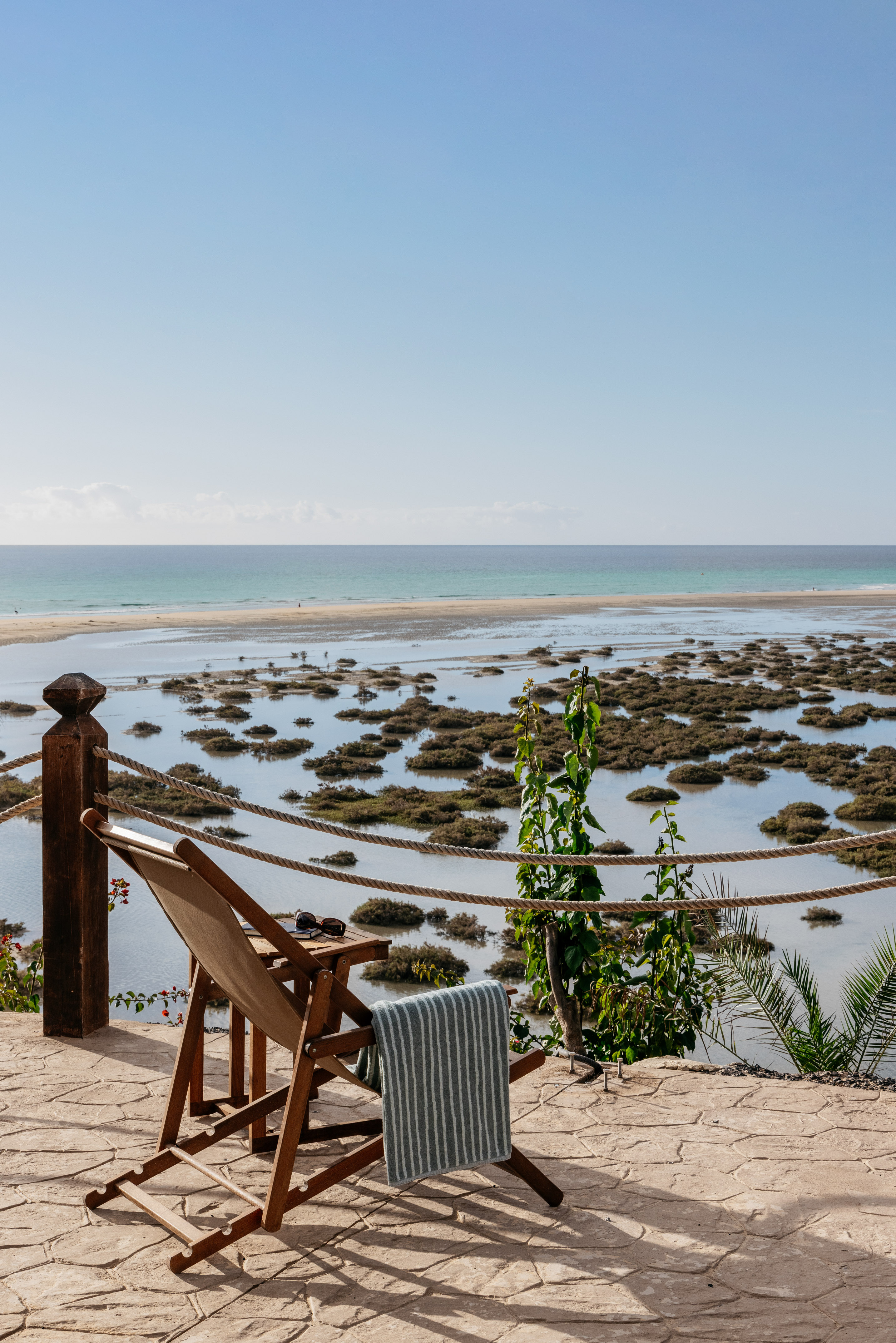 Deck chair with towel, sunglasses, overlooking beach, coastal lagoon, ocean.