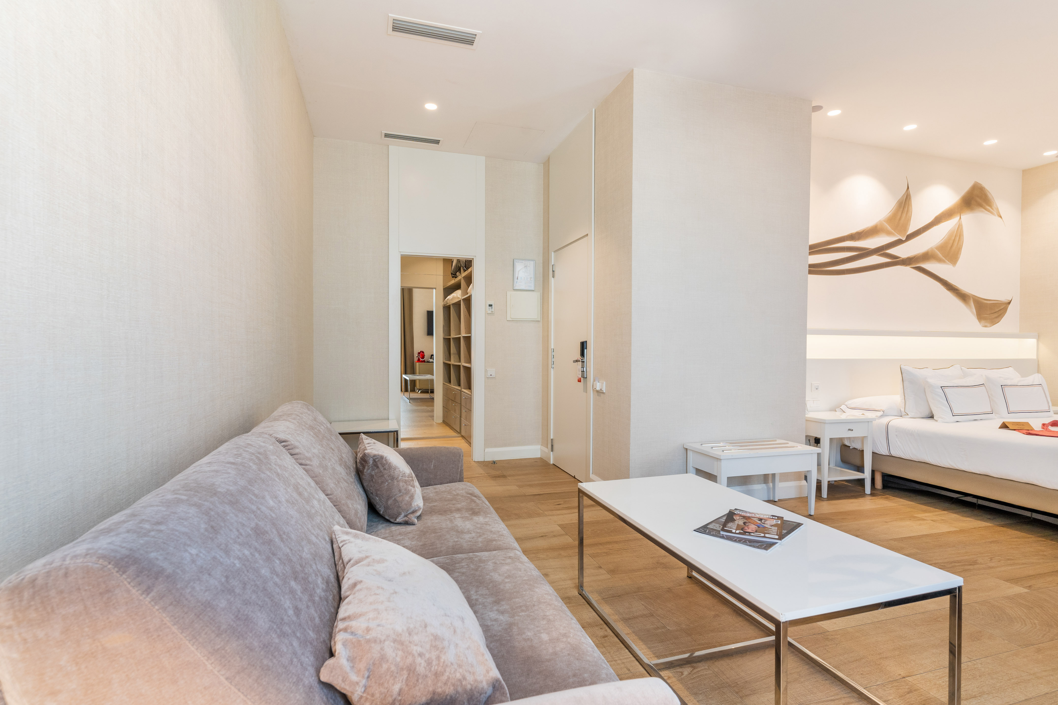 Modern hotel suite with living area, sofa, coffee table, and bedroom with floral art.