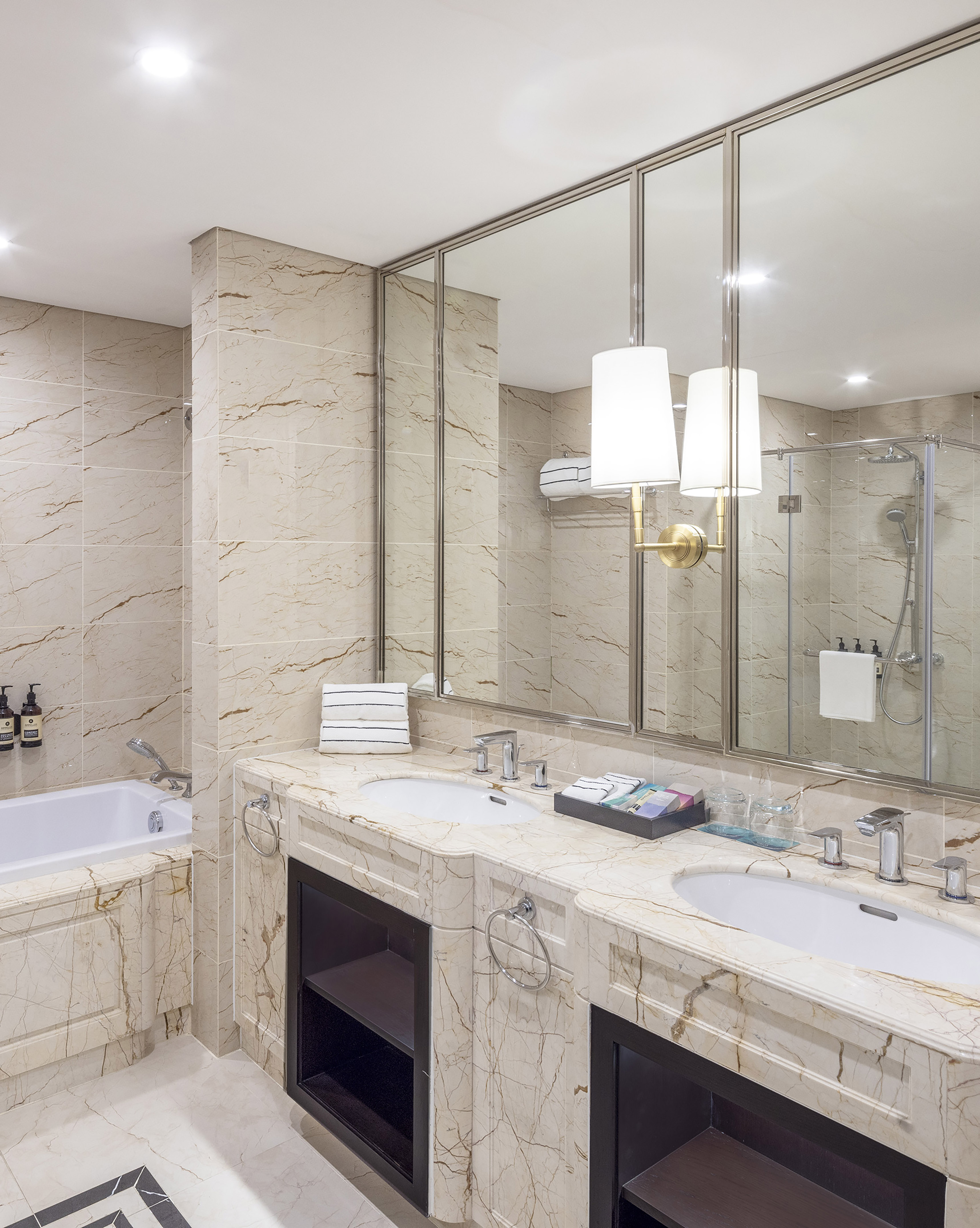 Luxury hotel bathroom with marble double vanity, bathtub, and glass shower.