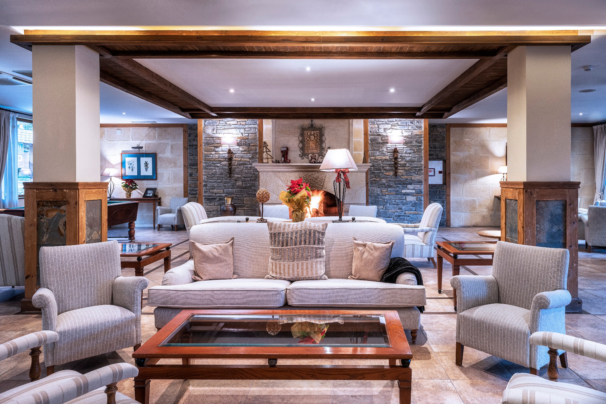 Cozy hotel lounge with stone fireplace, comfortable sofas, and rustic wooden beams.