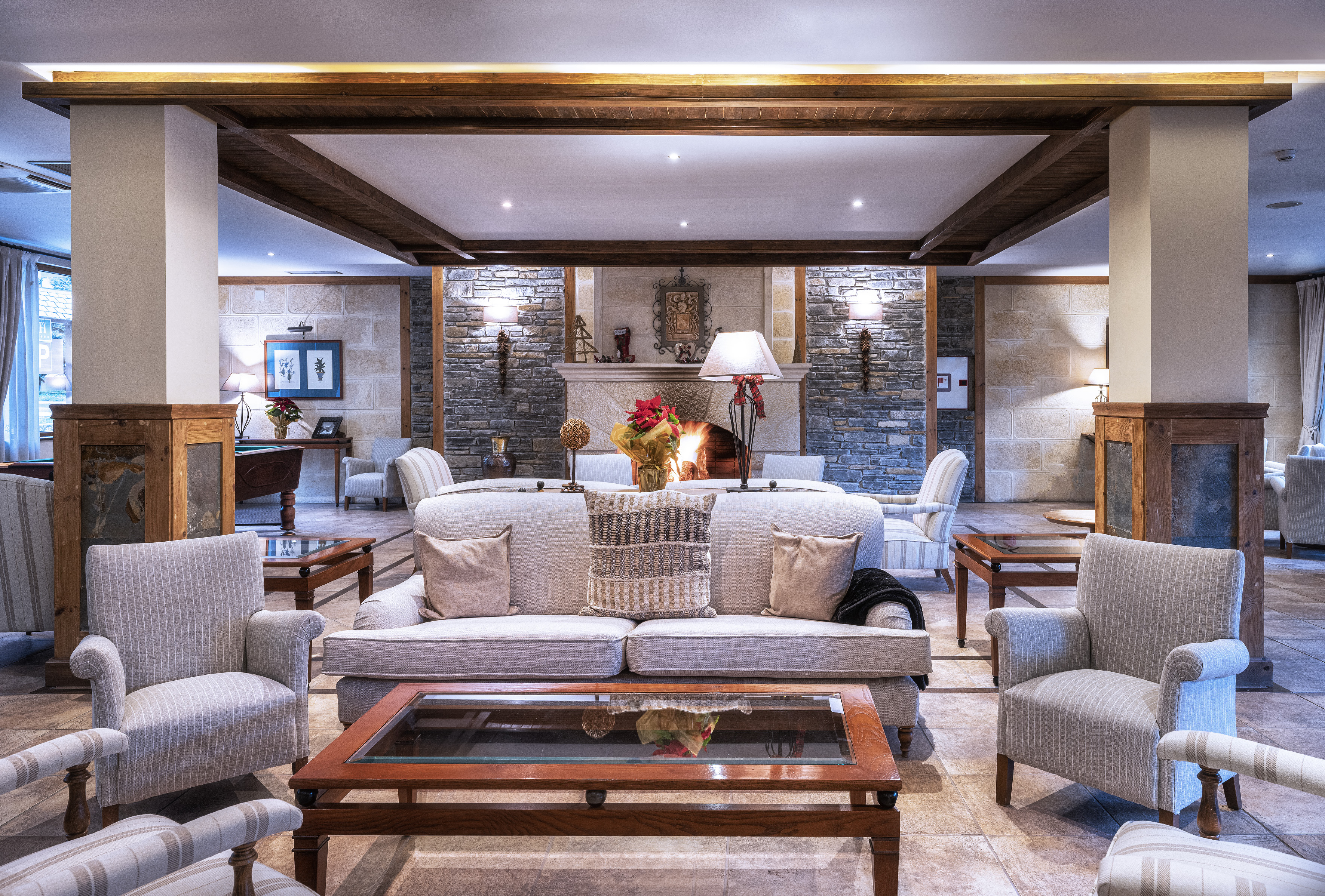 Cozy hotel lounge with stone fireplace, comfortable sofas, and rustic wooden beams.
