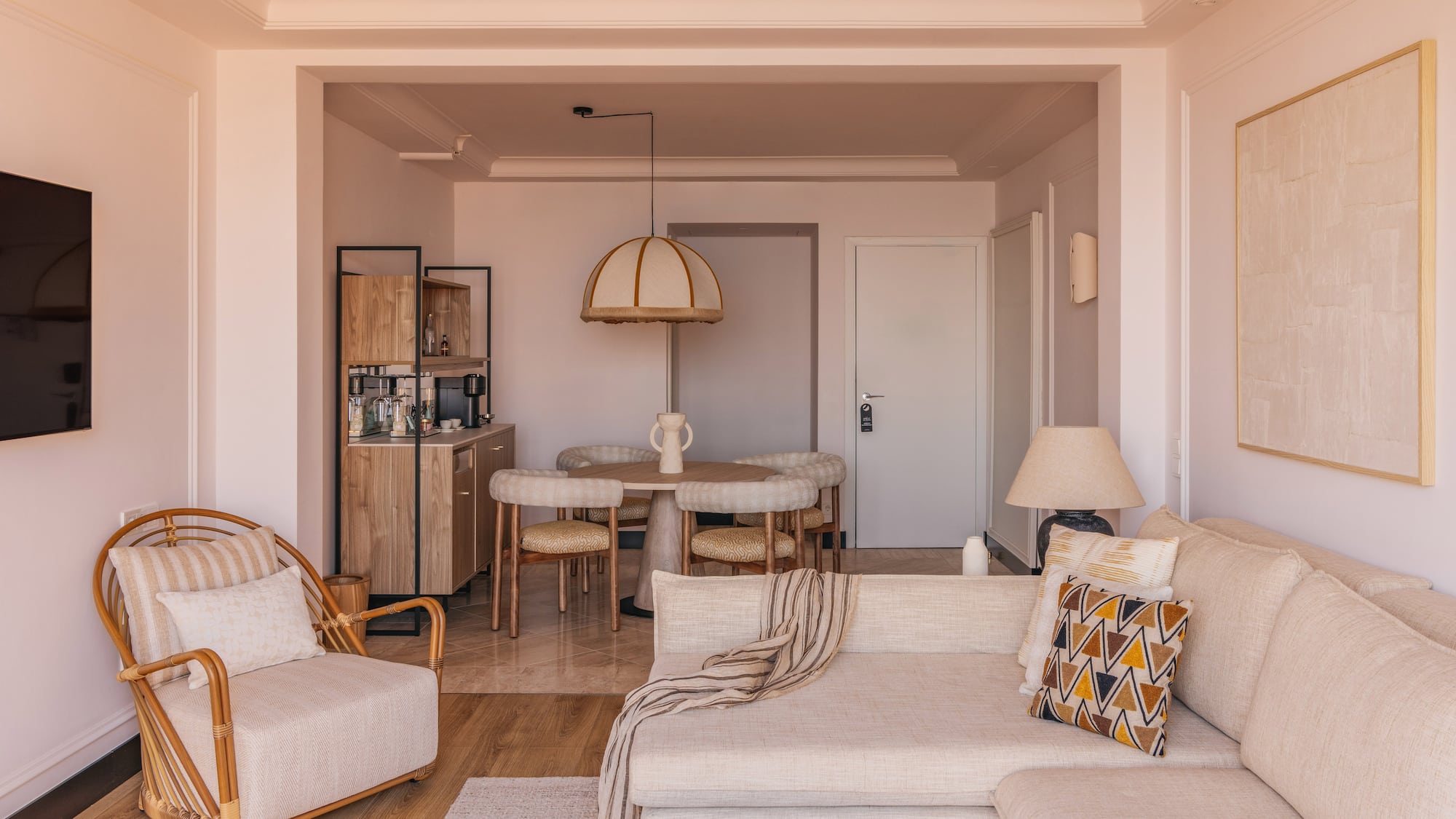 Modern neutral living room and dining area with sofa and rattan armchair.