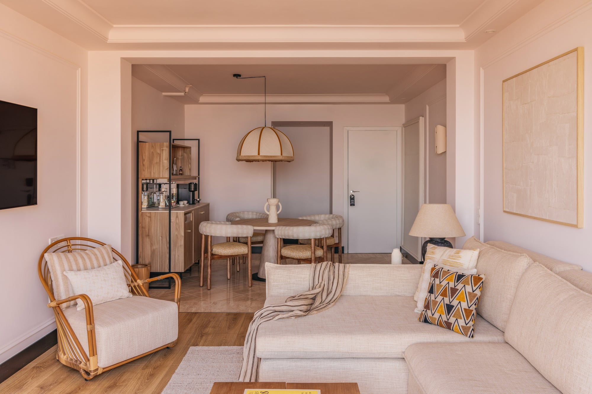 Modern neutral living room and dining area with sofa and rattan armchair.