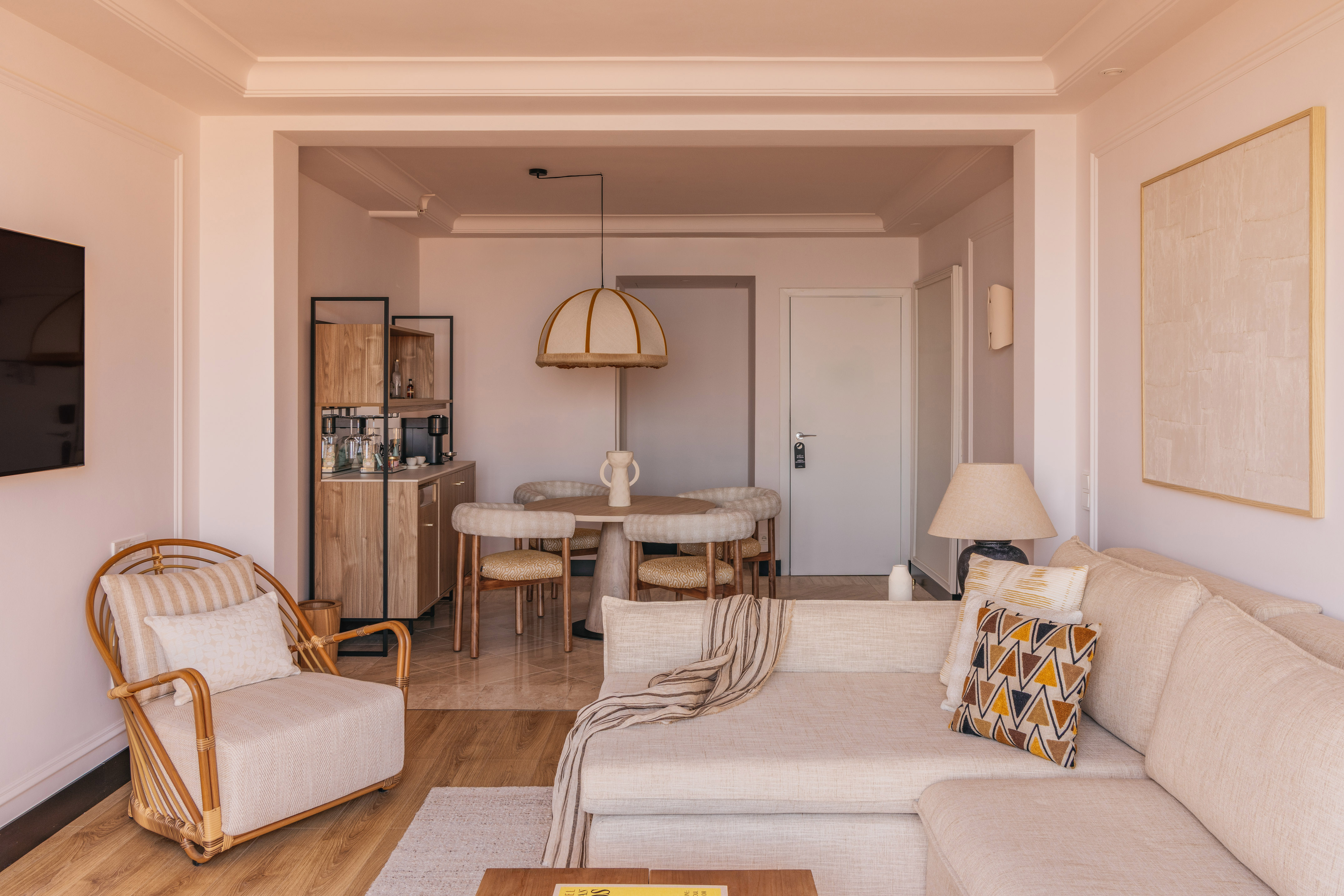 Modern neutral living room and dining area with sofa and rattan armchair.