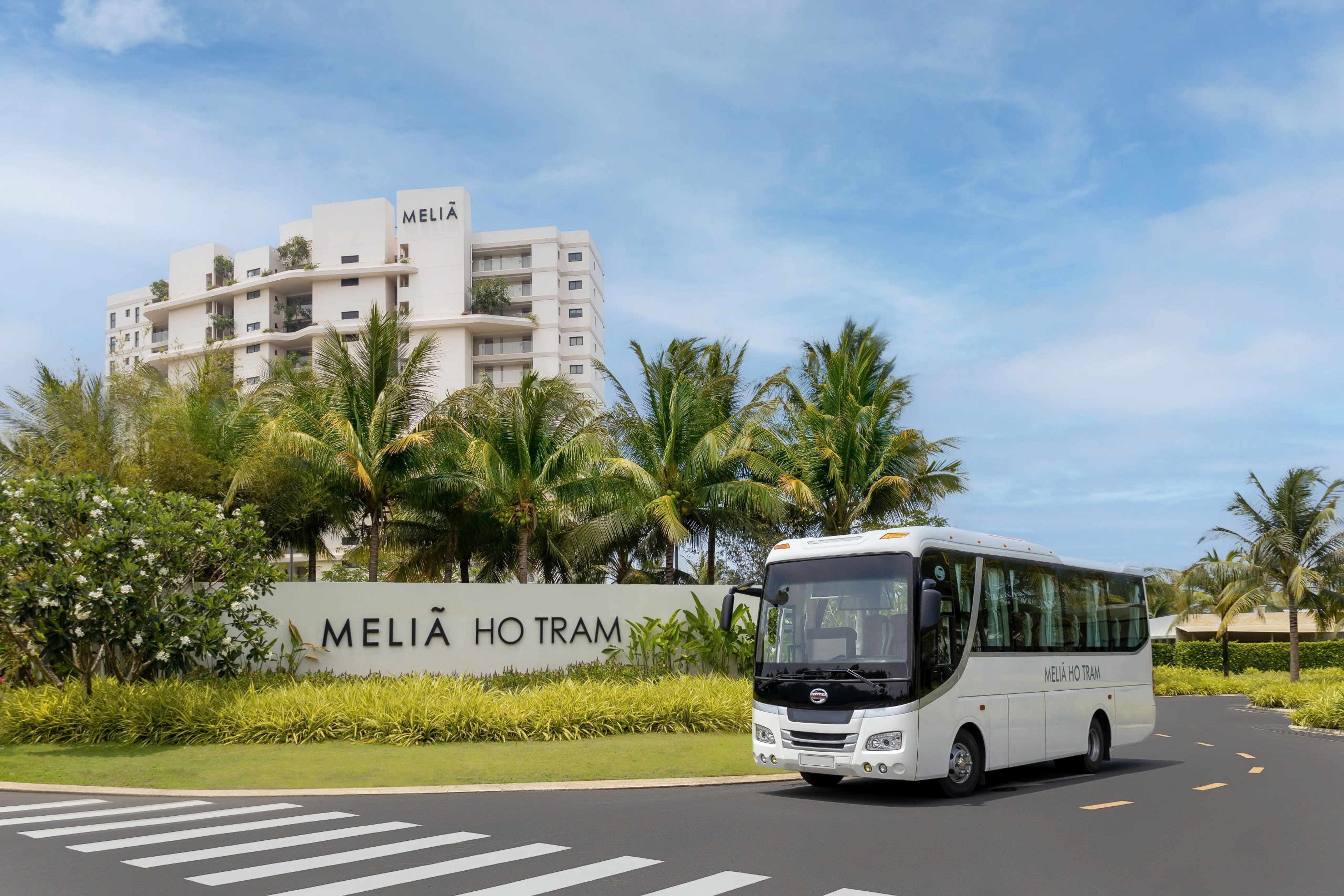 Melia Ho Tram hotel exterior with white shuttle bus and tropical landscaping.