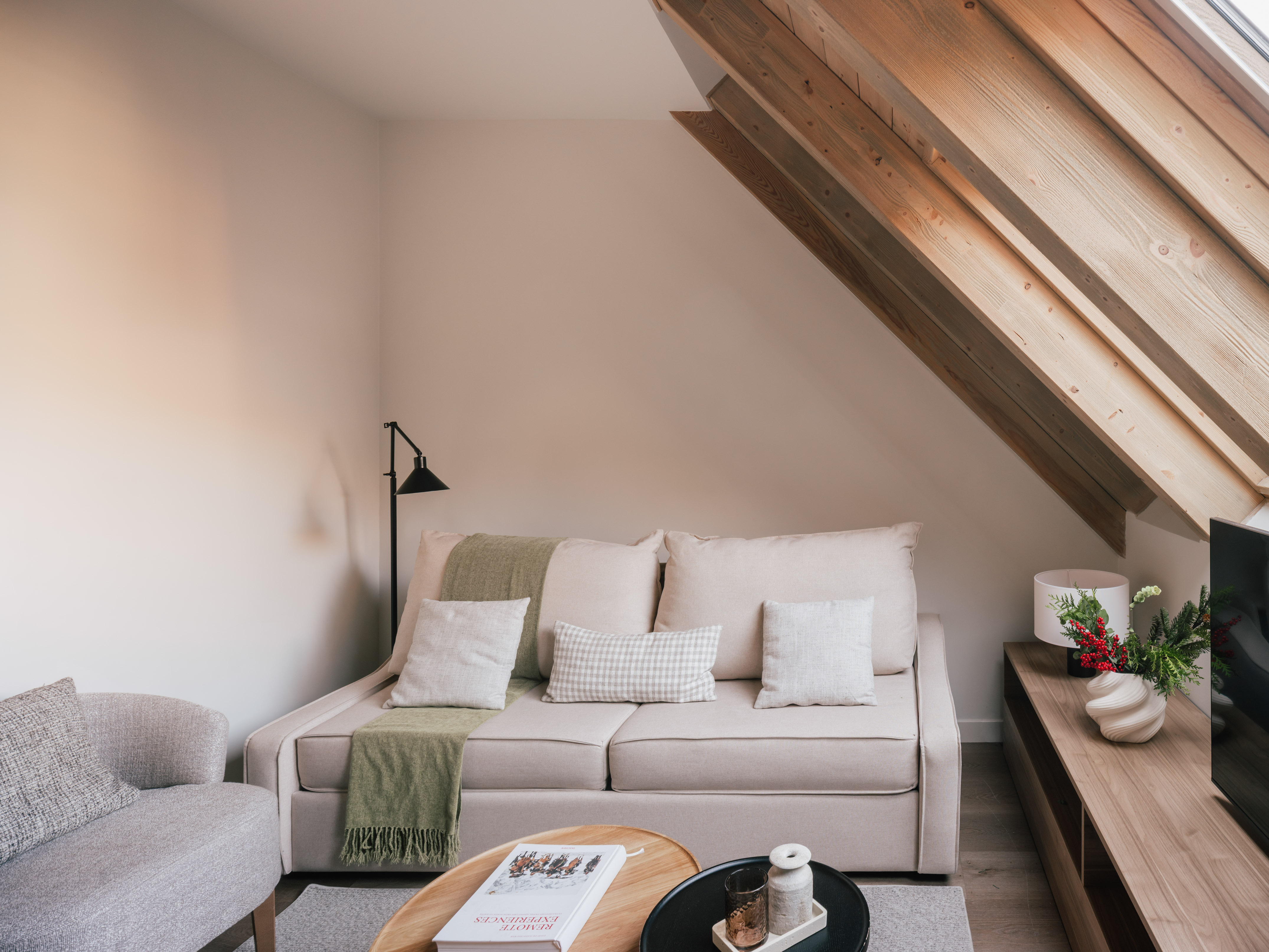 Modern attic living room with beige sofa, wooden beams, and neutral decor.