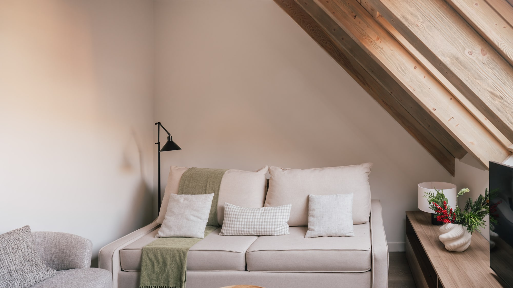 Modern attic living room with beige sofa, wooden beams, and neutral decor.