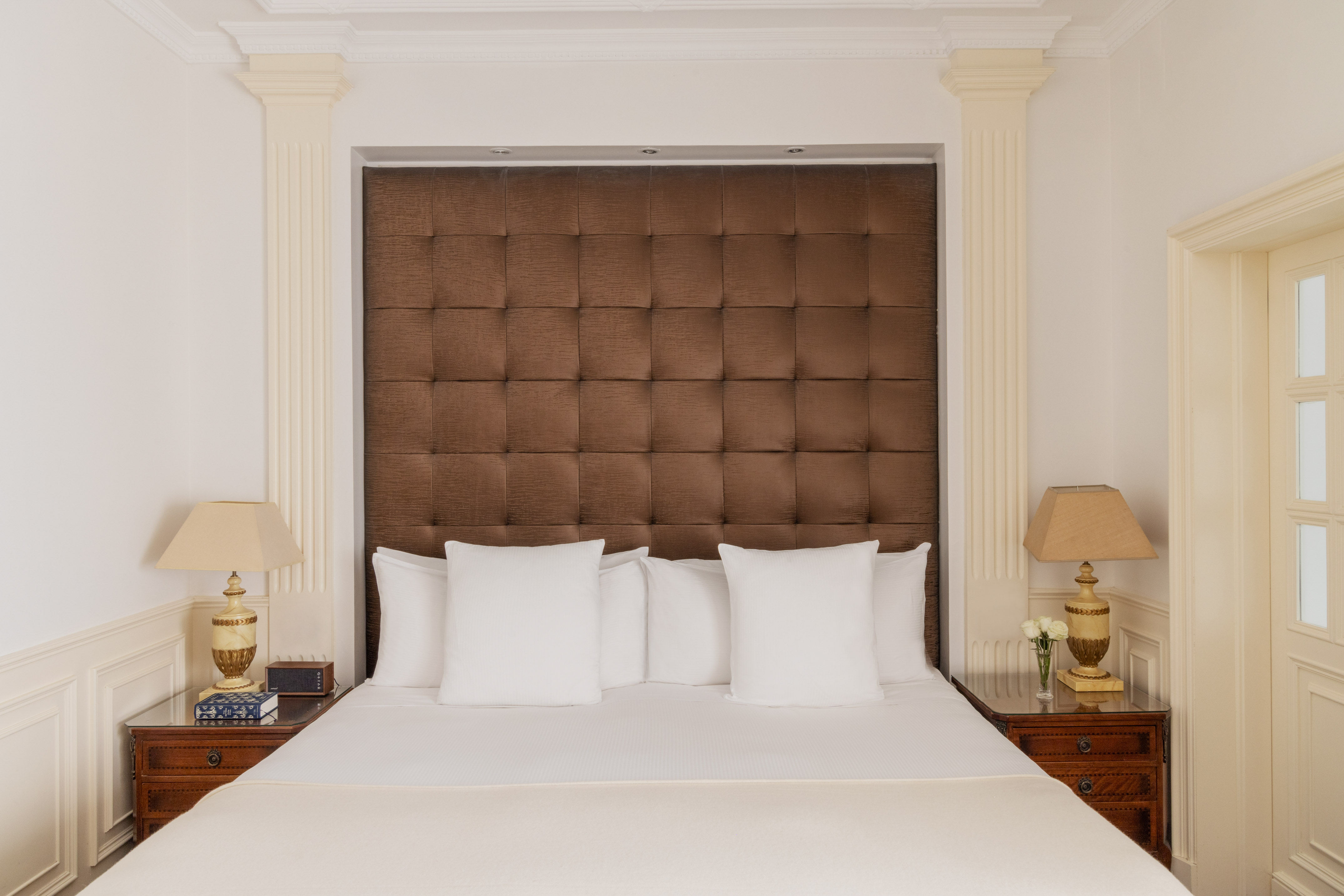 Elegant hotel room with tufted brown headboard, white bed, classic nightstands.